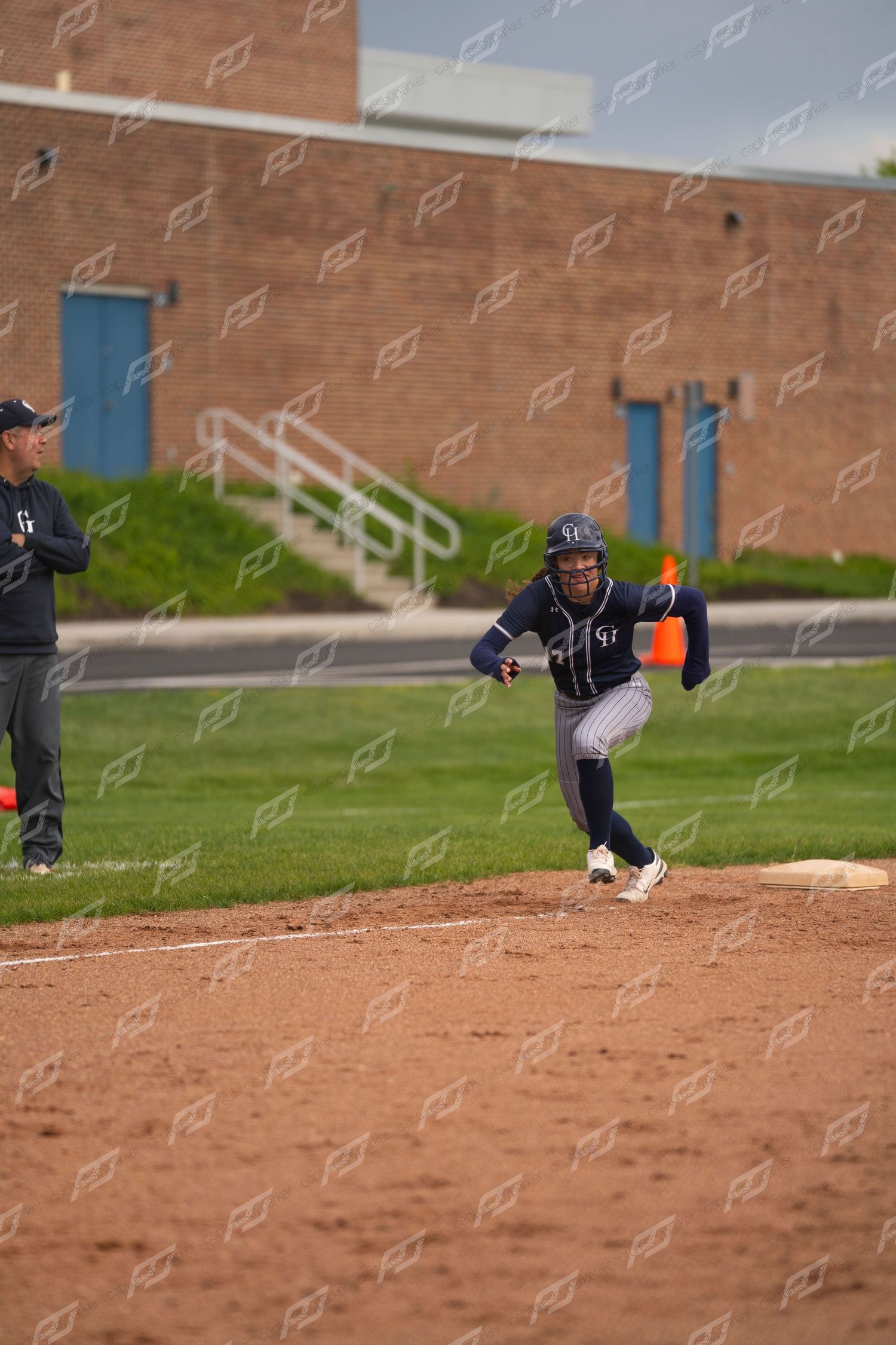 Female softball player sprints from first base in navy pinstripe uniform during a game.