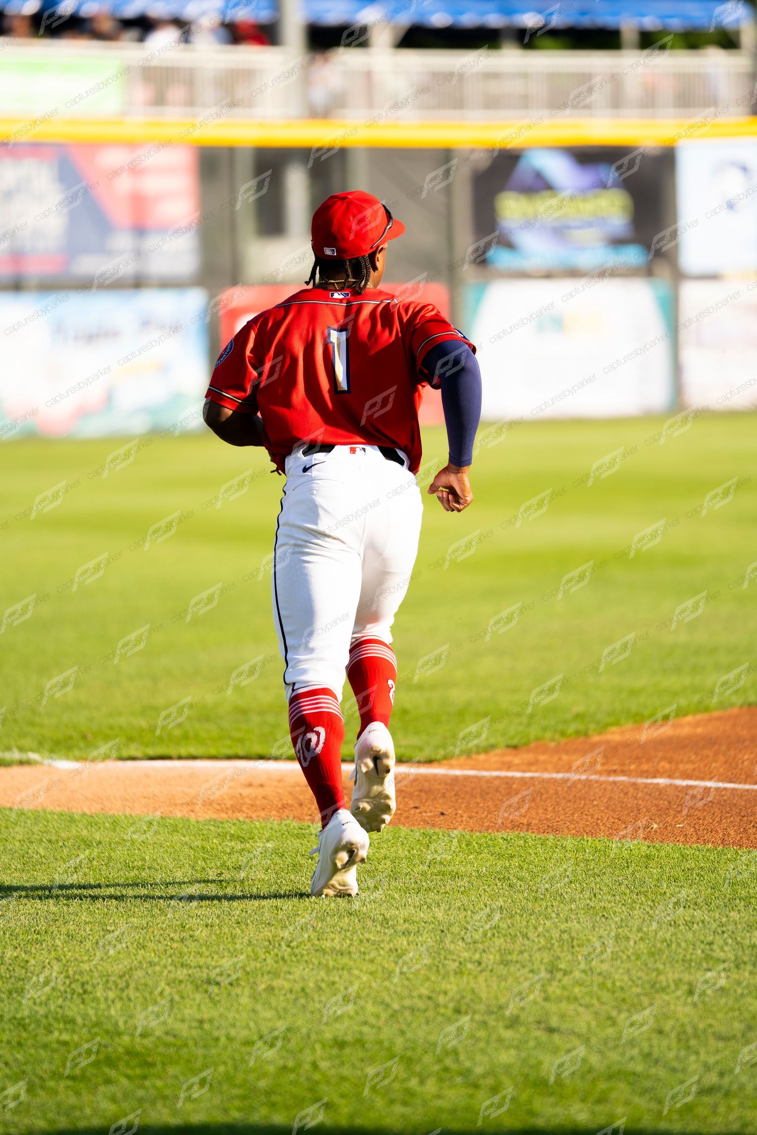 Baseball player #1 in red uniform running toward base on a sunny day at the ballpark.