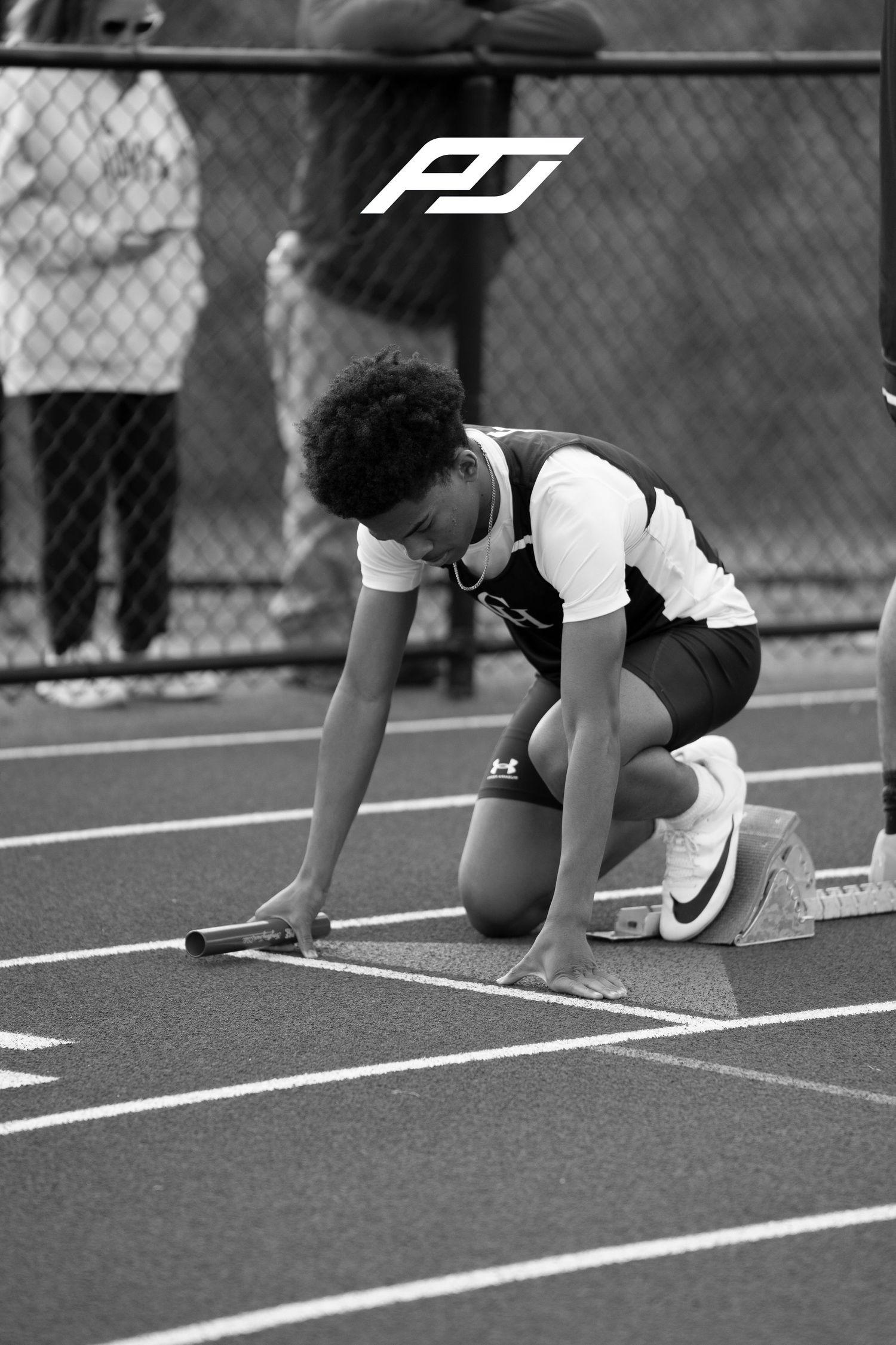 Young relay runner crouches in starting position holding baton on outdoor track lane.