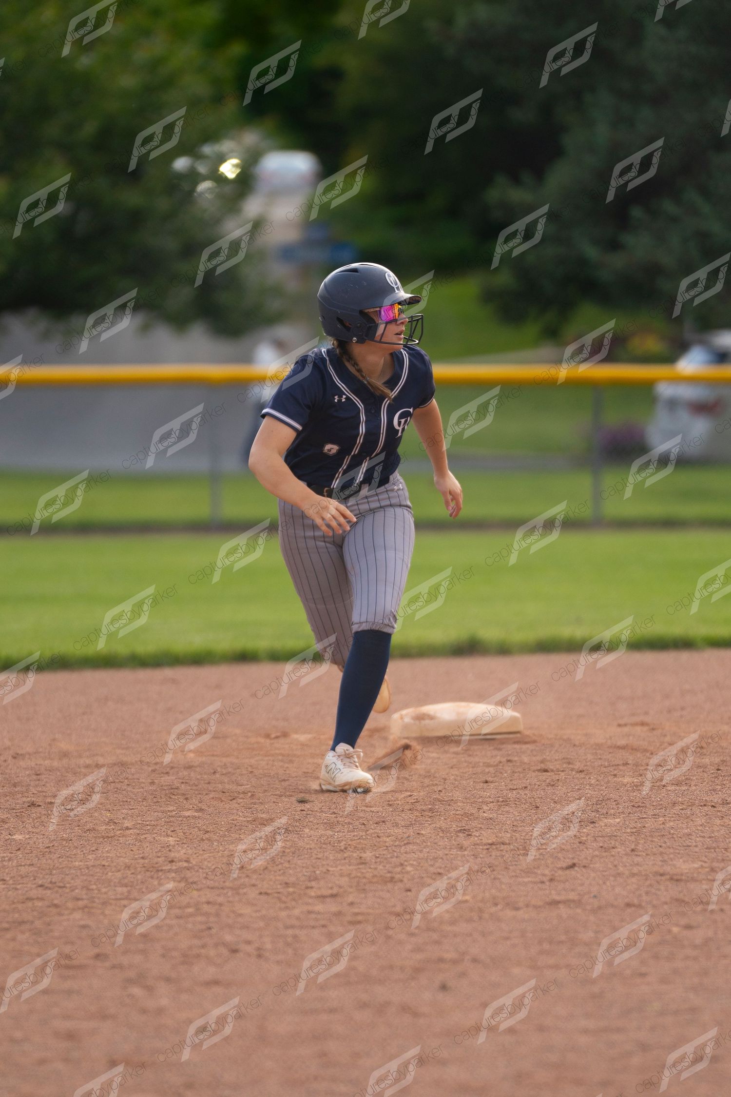 Softball player in navy pinstripe uniform rounds second base during a competitive game.