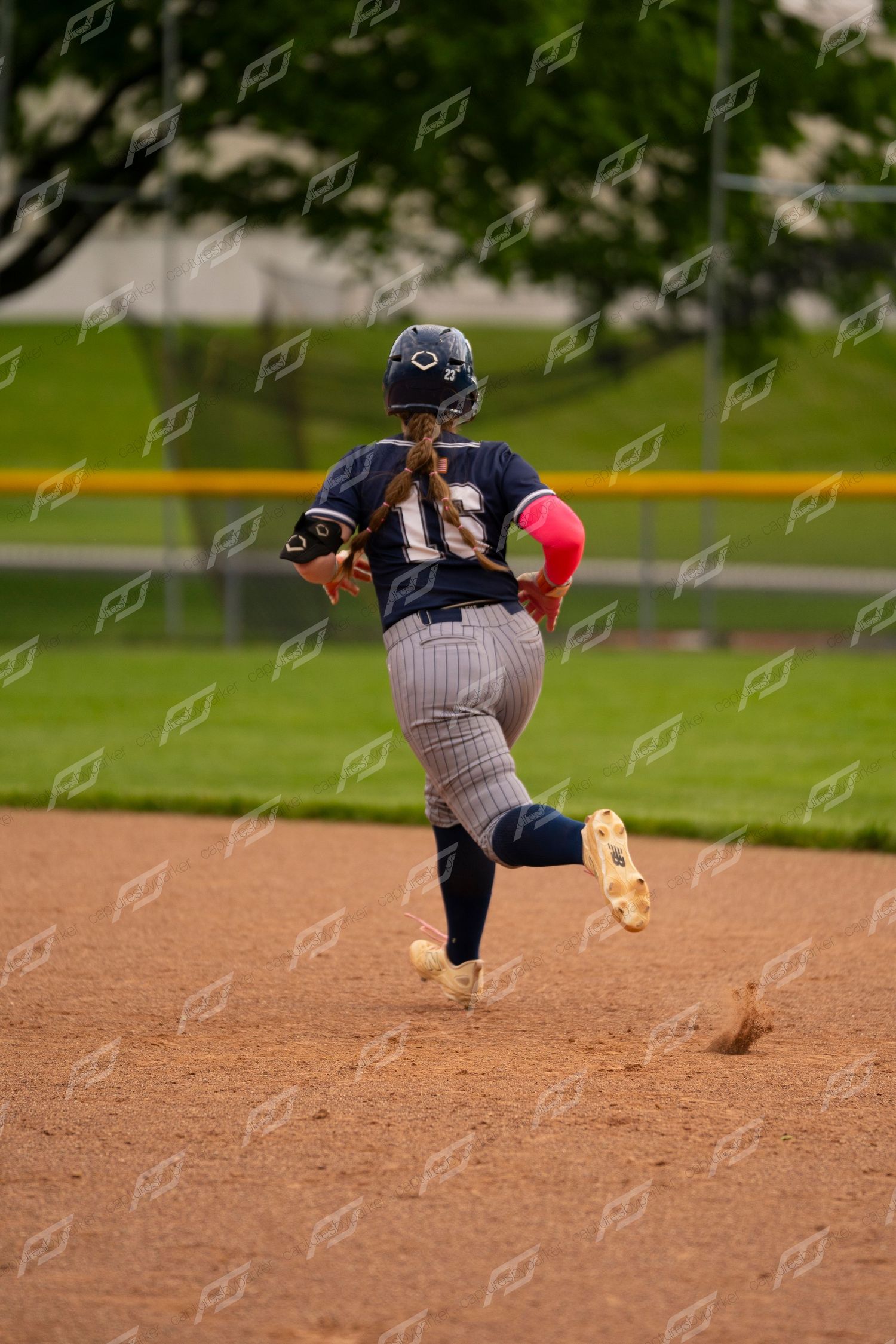 Female softball player in navy pinstripe uniform runs bases during a game.