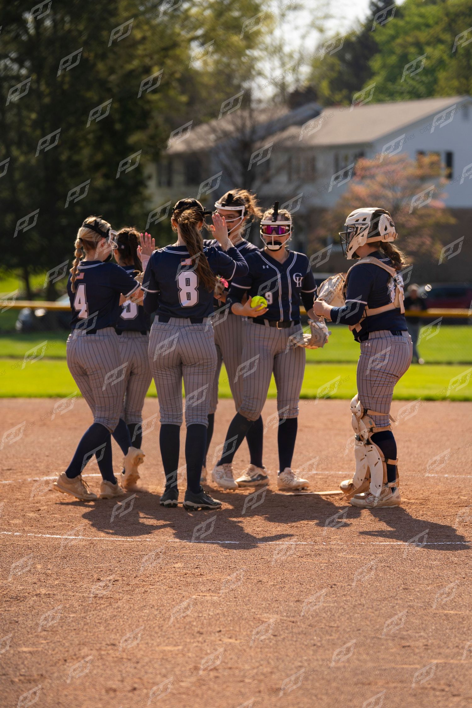 Softball team in navy pinstripe uniforms huddles together on the field during a game on a sunny day.
