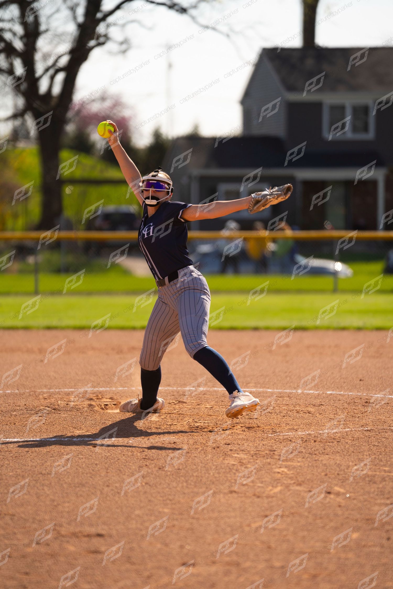 Softball pitcher in navy uniform winds up with ball raised high on the mound.