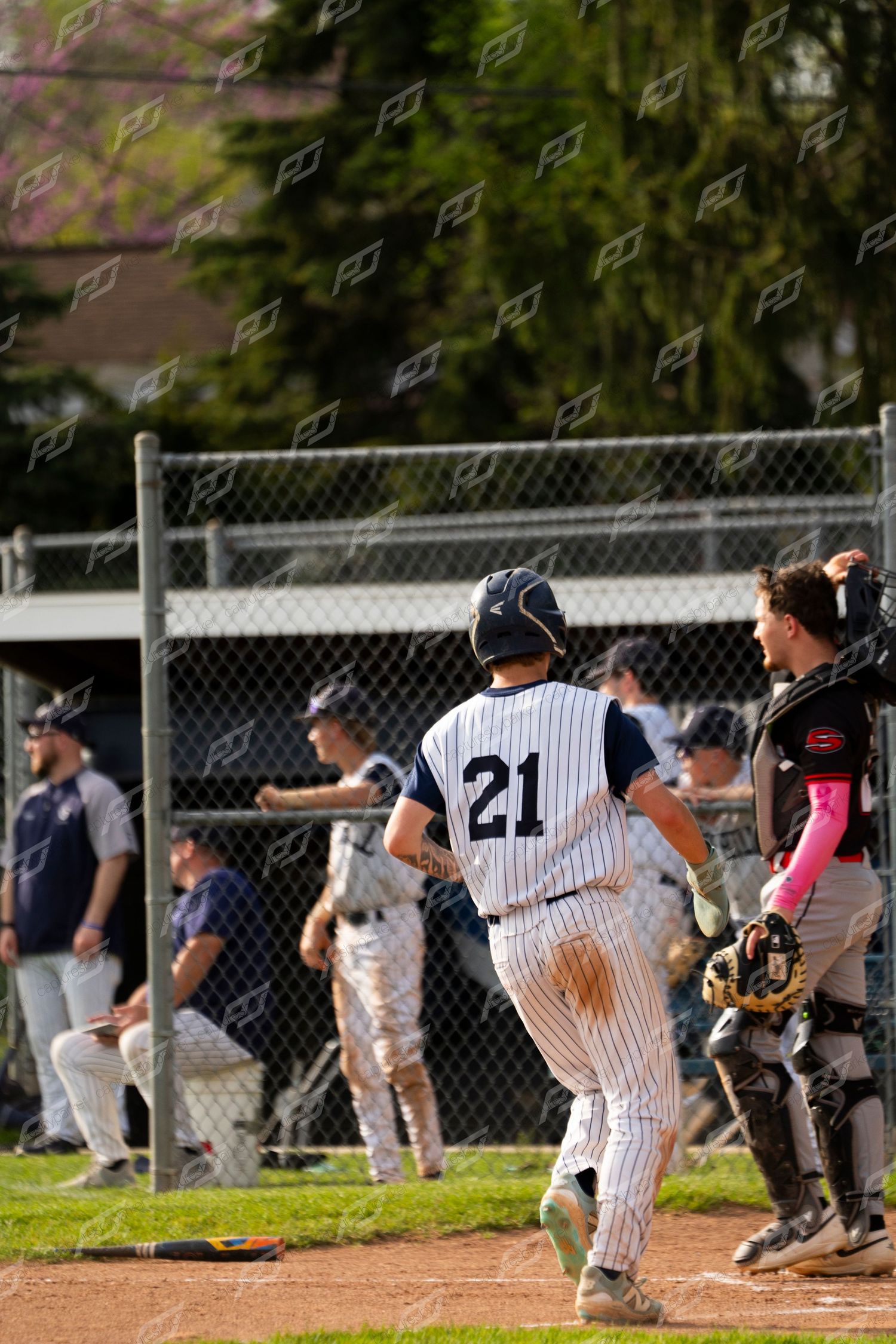 Baseball player #21 in pinstripe uniform runs toward home plate as catcher waits during a youth baseball game.