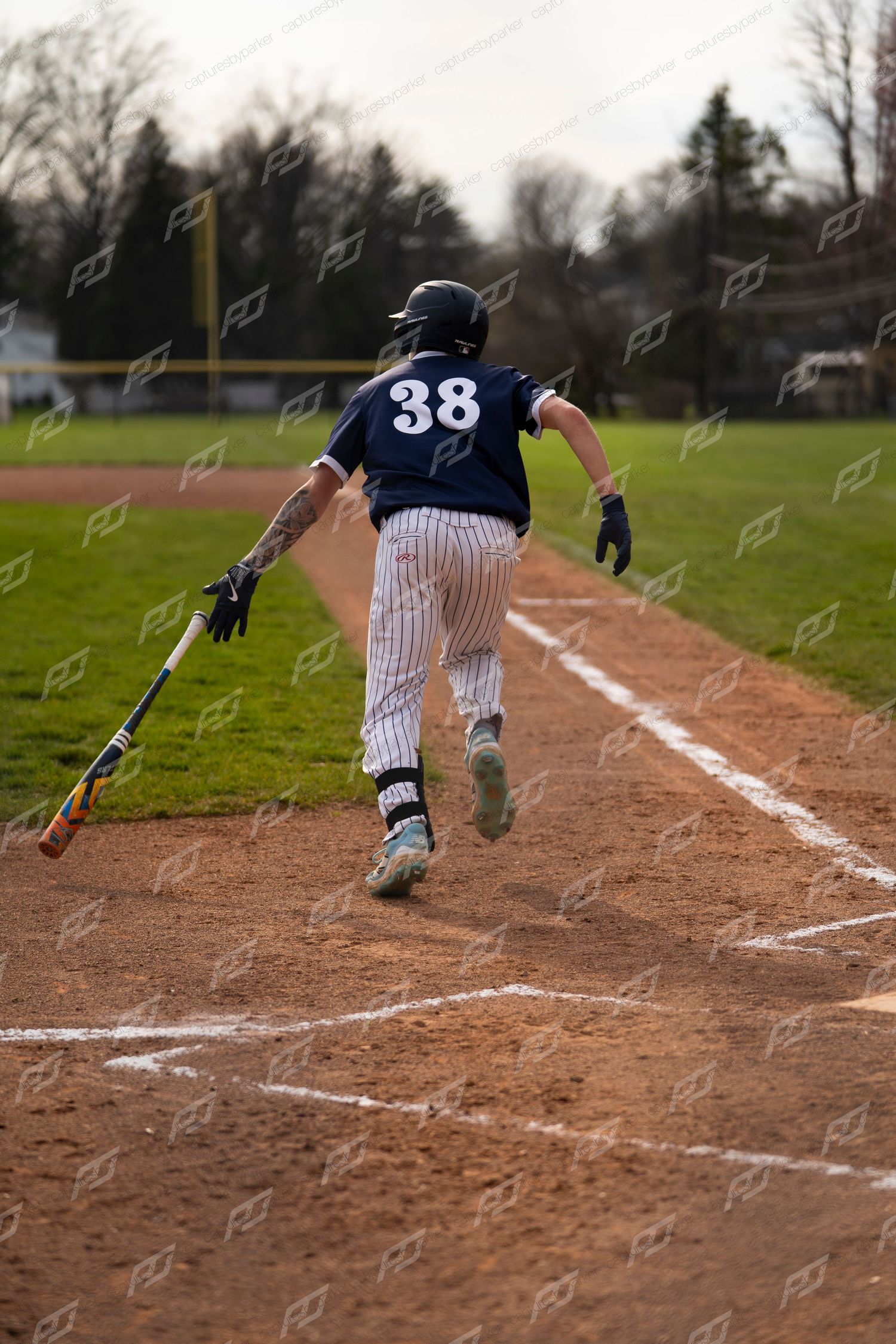 Baseball player #38 in navy uniform drops bat and sprints from home plate.