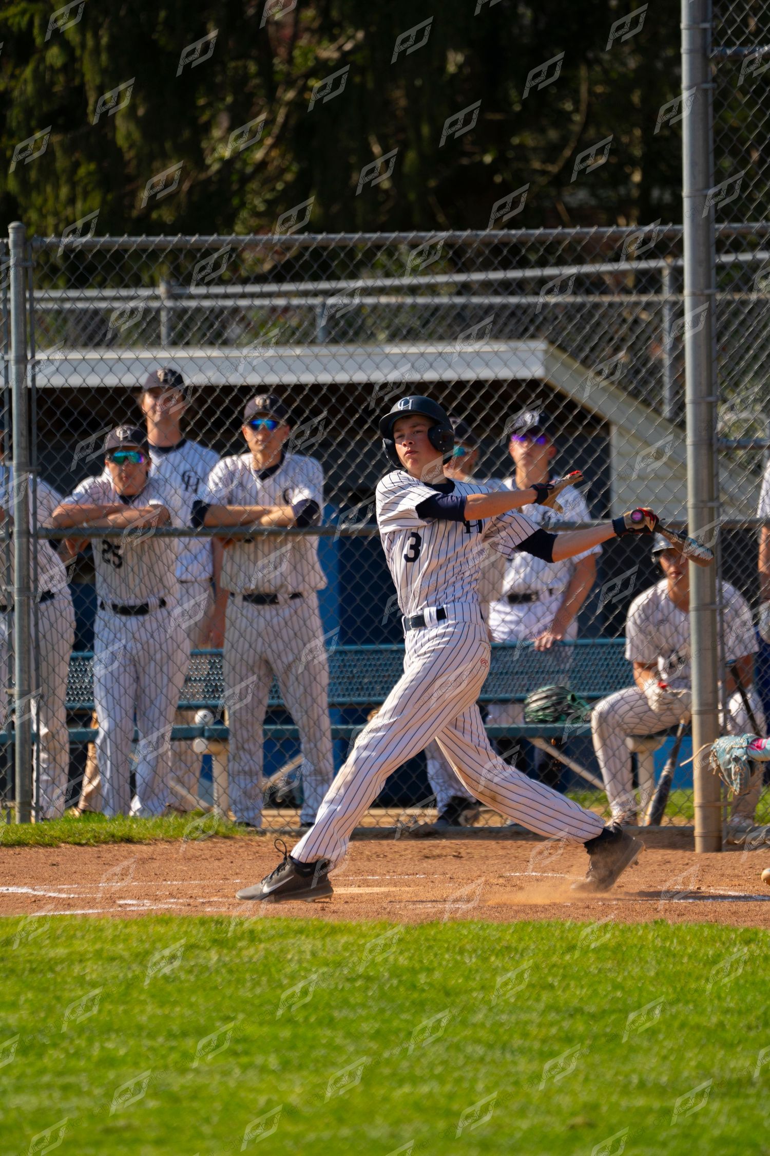 Baseball batter in pinstripe uniform swings while teammates watch from dugout fence.