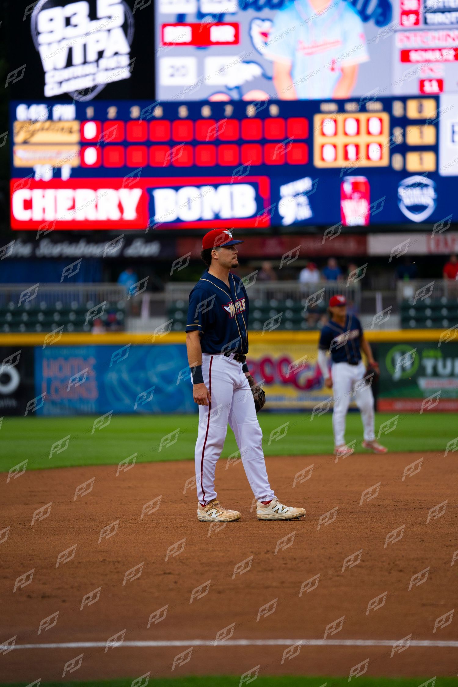 Minor league baseball player standing at second base with Cherry Bomb scoreboard lit up behind him.