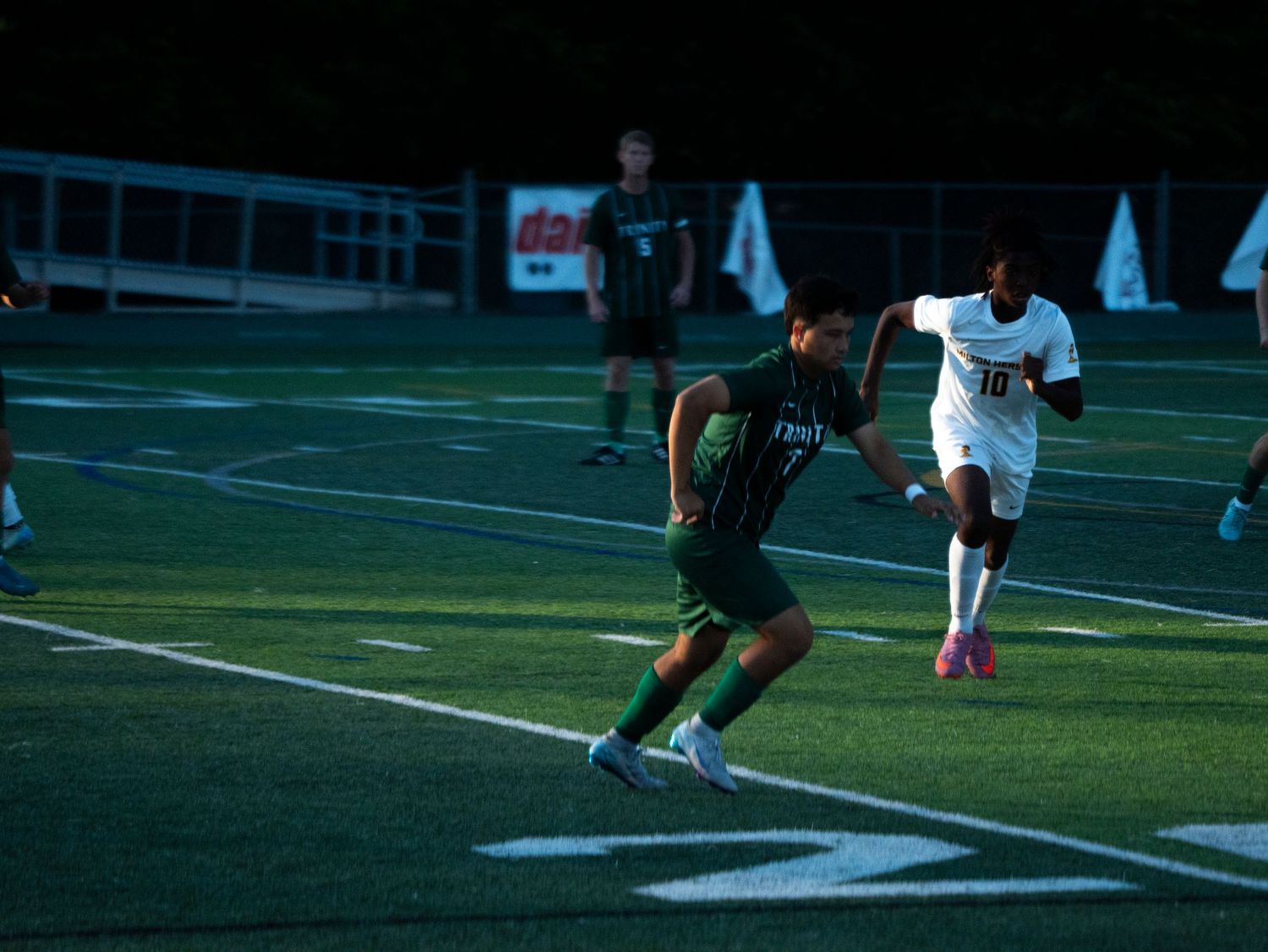 Two soccer players compete for the ball on a turf field during an evening high school soccer game.