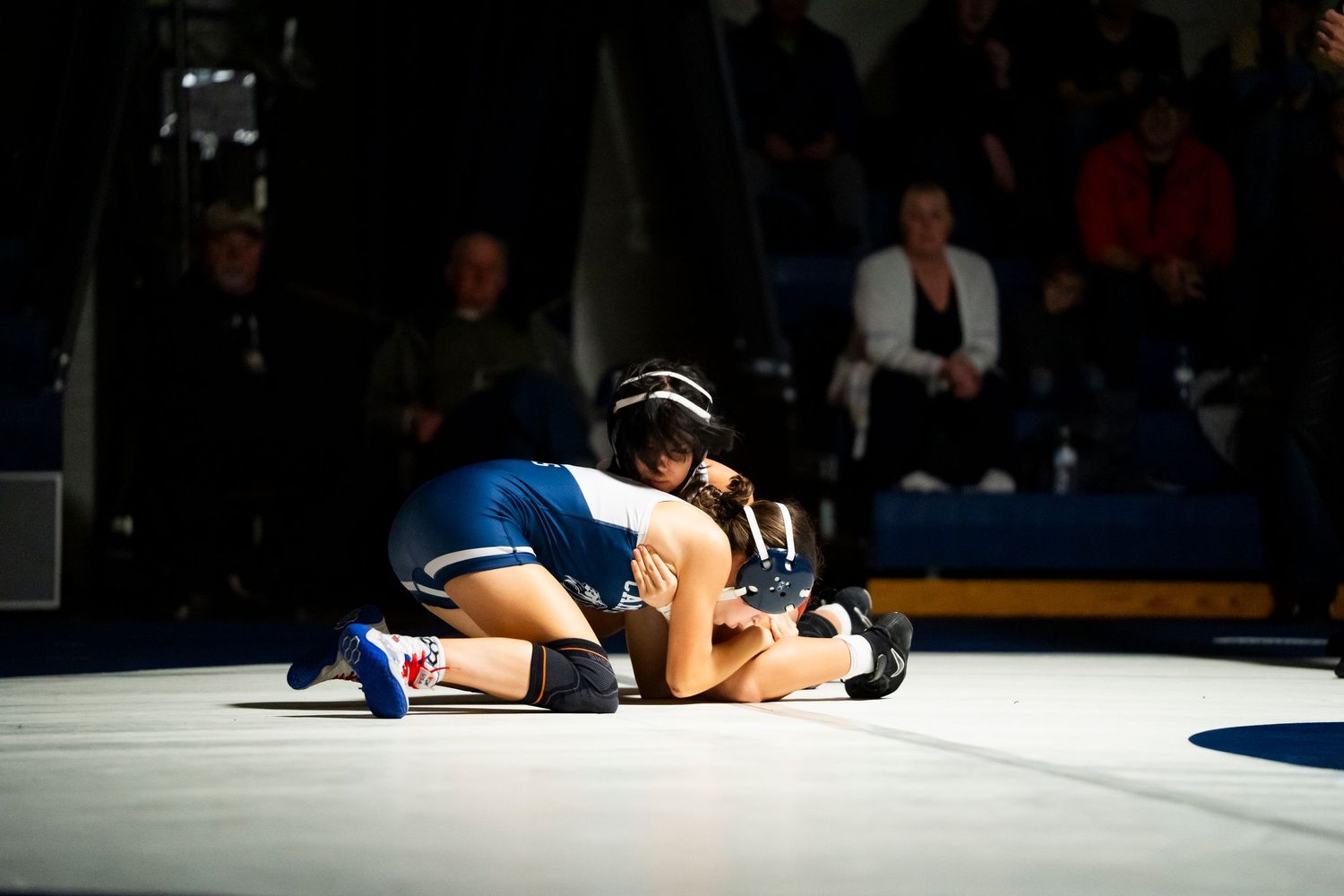 A wrestler attempts to pin their opponent on a blue wrestling mat.