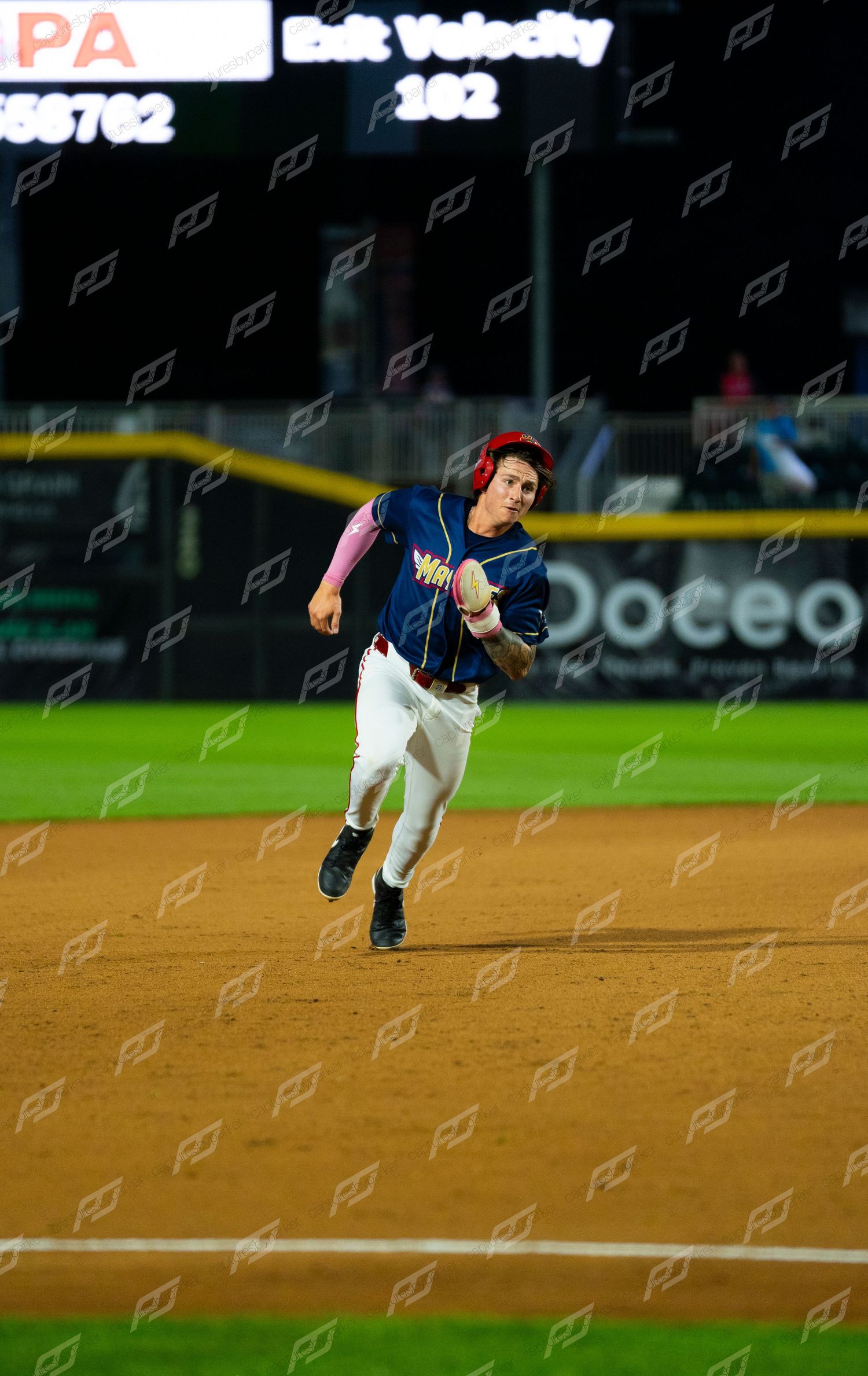 Baseball player rounds the bases at full speed with exit velocity of 102 displayed on scoreboard.