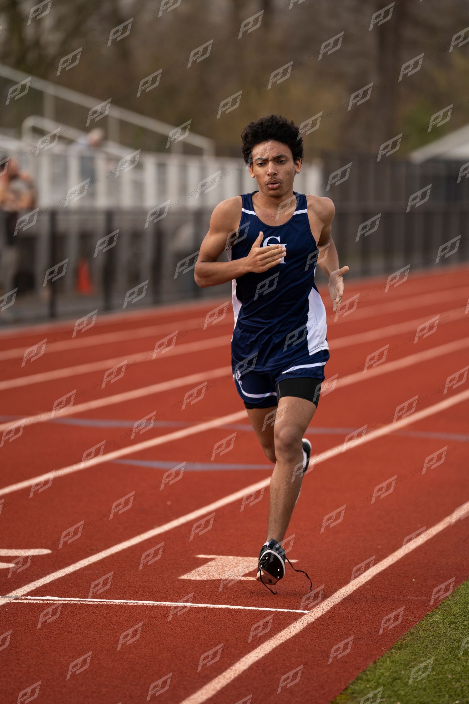 Male CH track athlete in navy uniform running on red track during race.