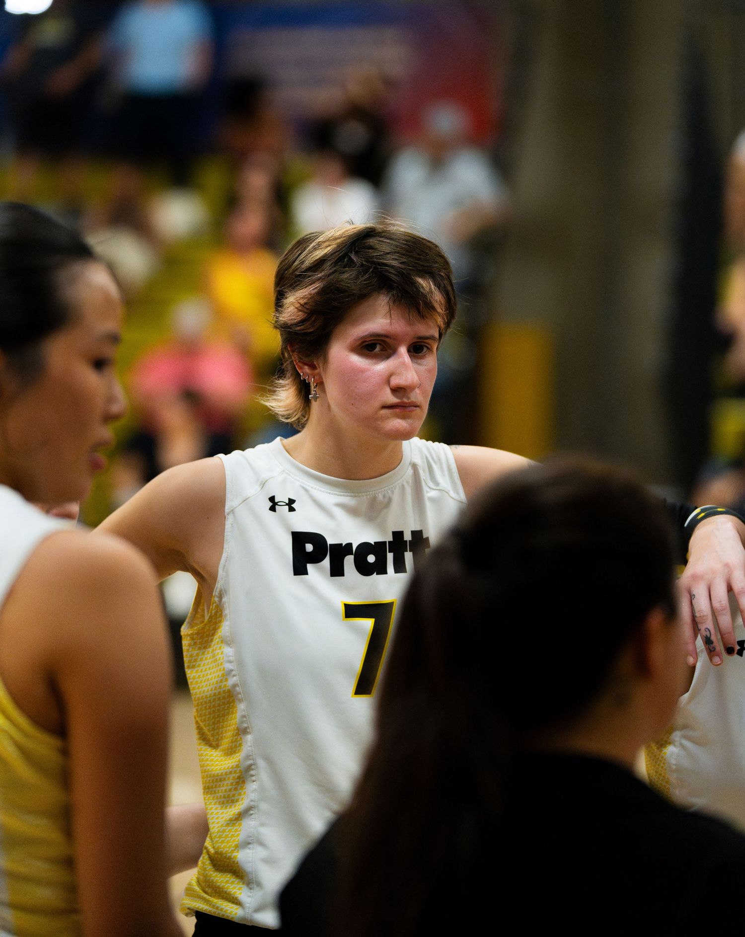 Pratt volleyball player #7 listens intently during a timeout huddle wearing a white Under Armour jersey.