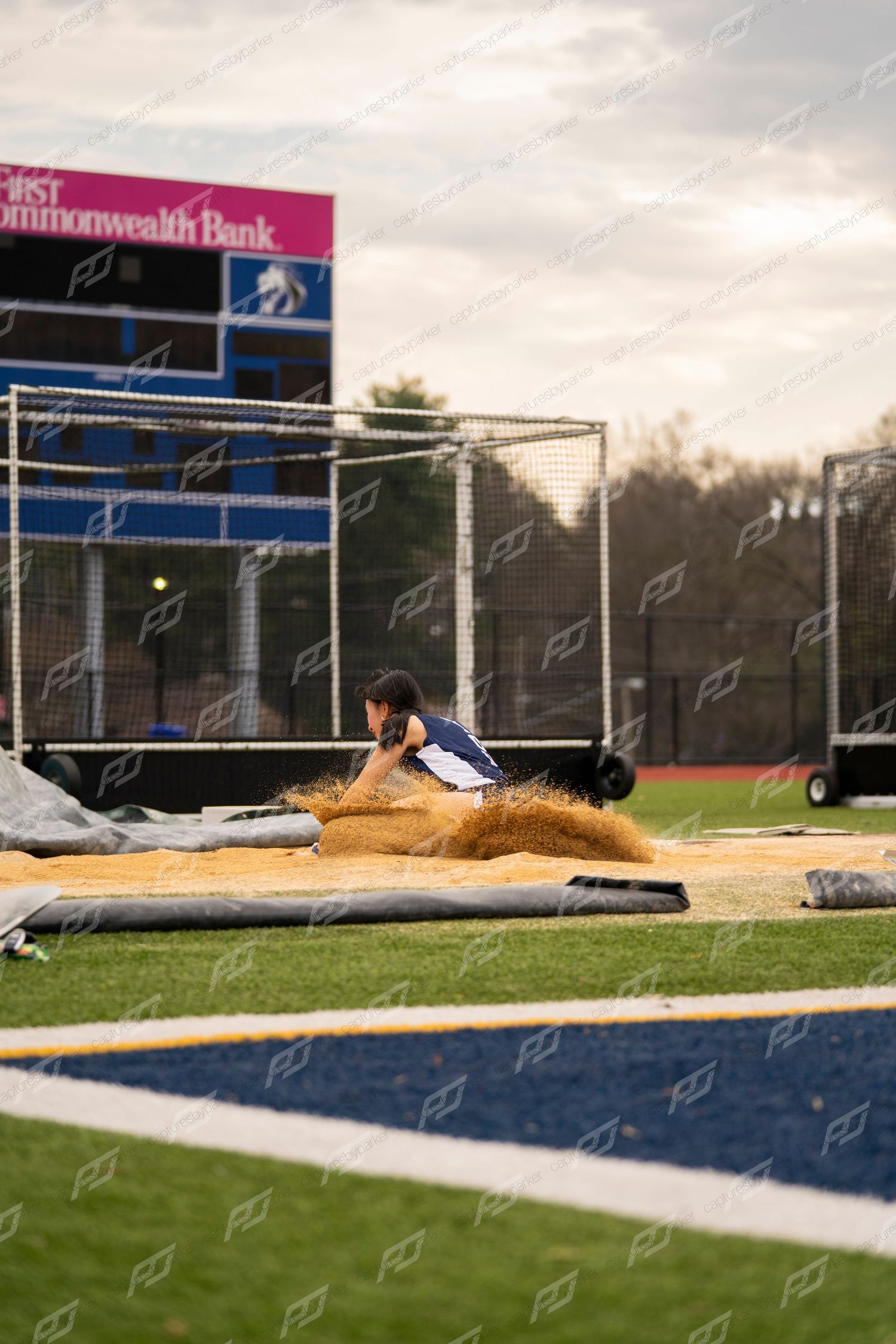 A track and field athlete lands in the sand pit during a long jump event at an outdoor meet.