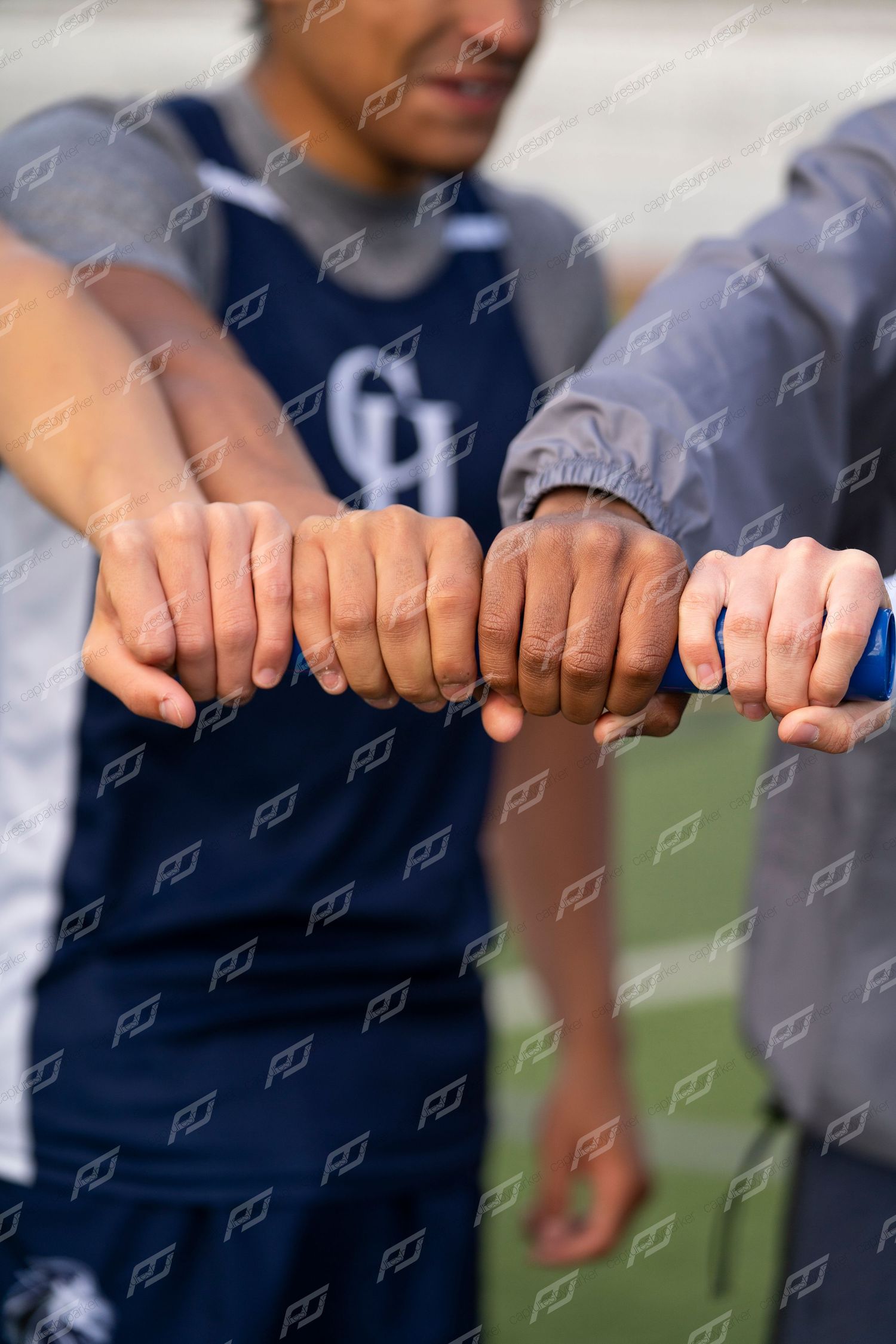 Athletes extend fists together in a team unity gesture on a sports field.