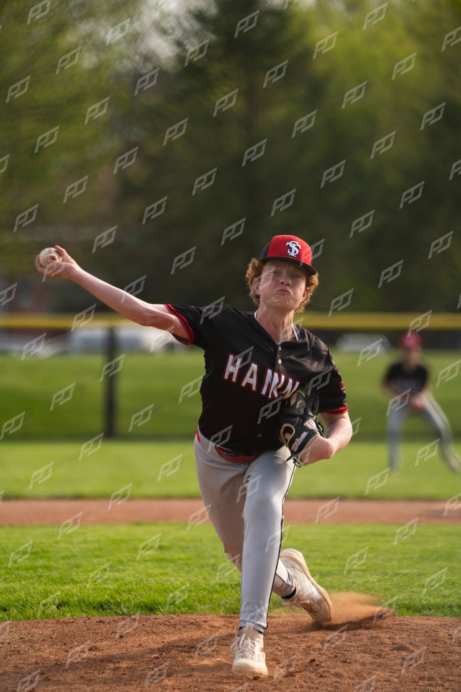 Hanna baseball pitcher in black uniform delivering a pitch from the mound during a sunny outdoor game.