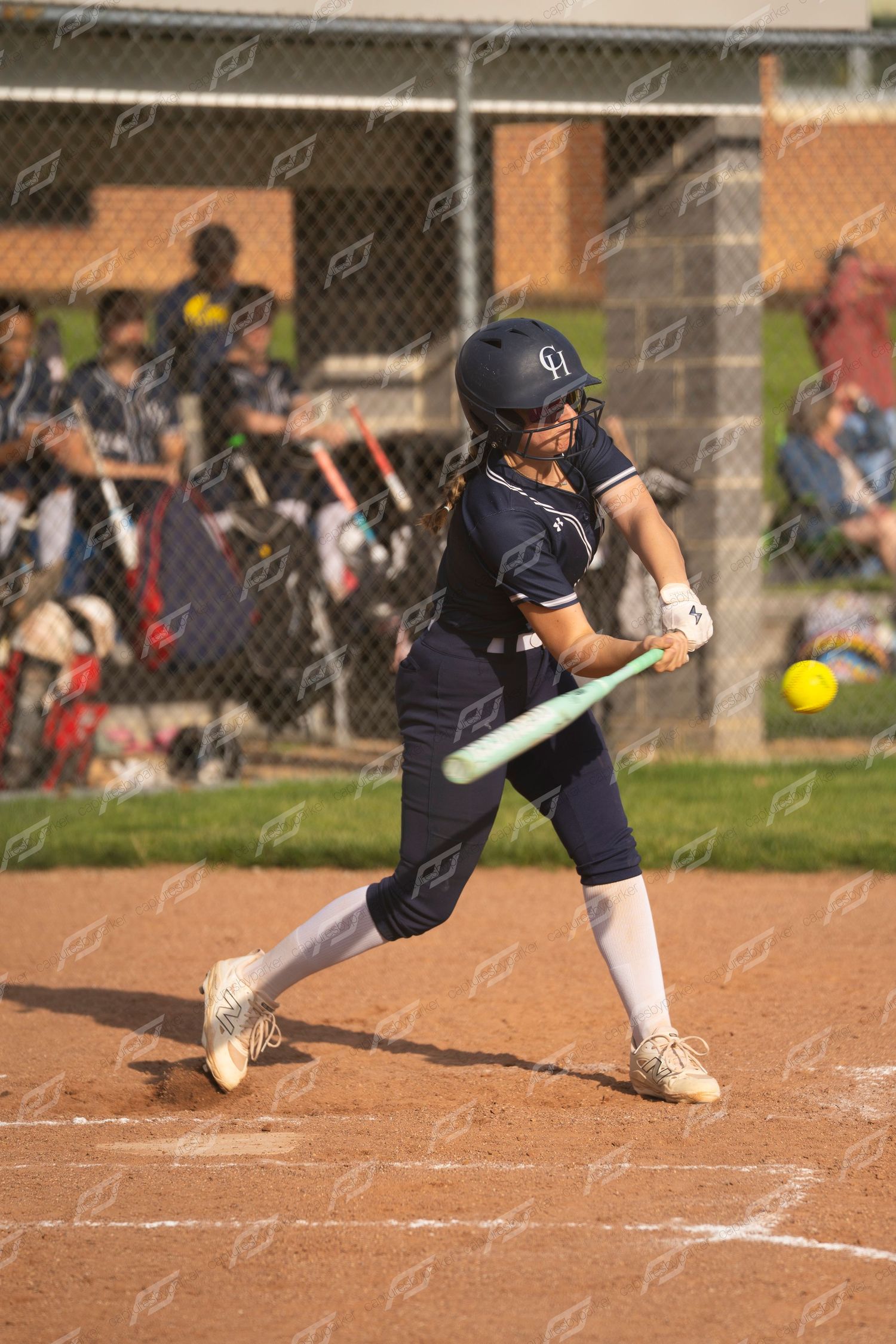 Softball batter in navy uniform makes contact with a yellow ball during a game.