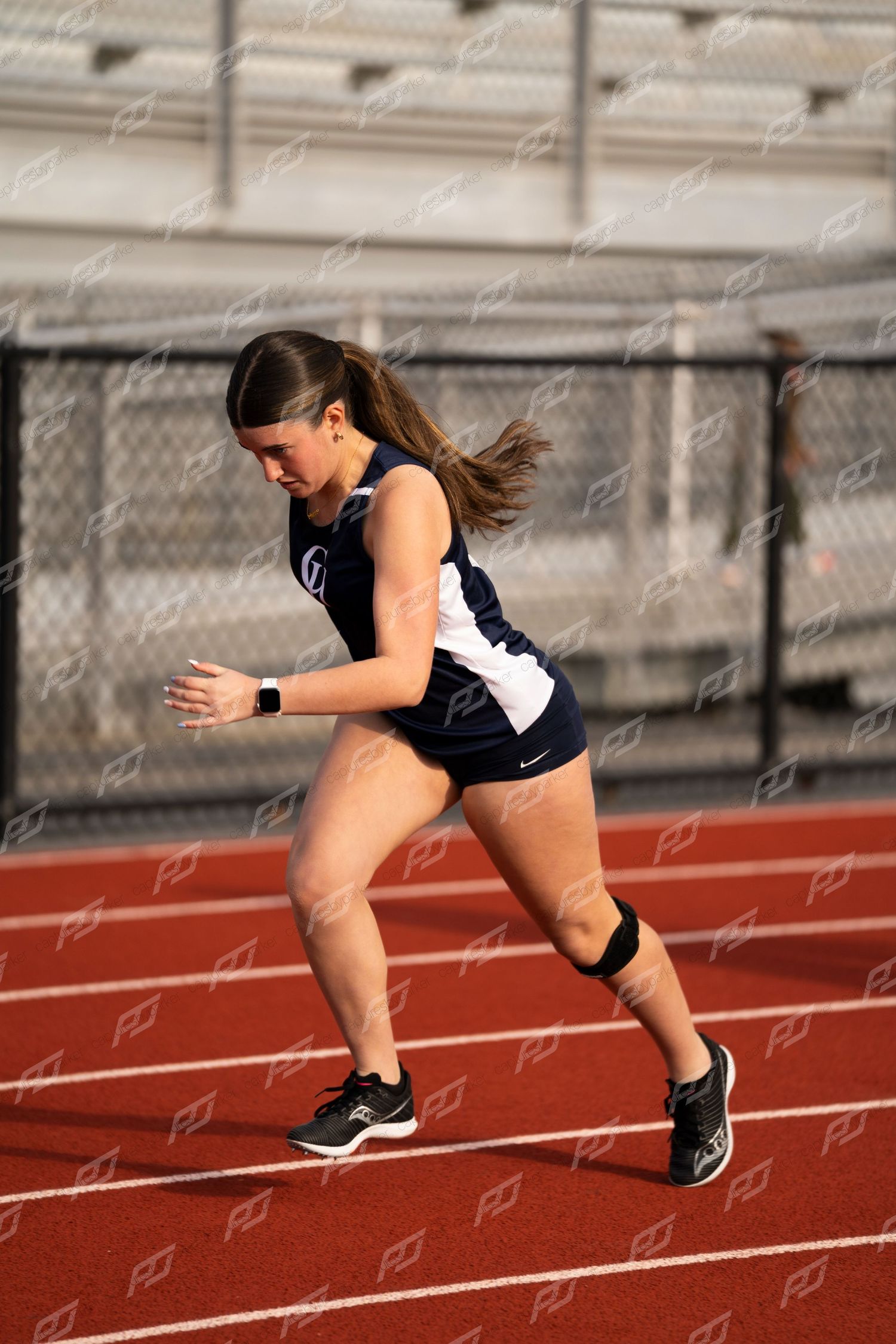Female high school track athlete exploding out of starting position on red track.