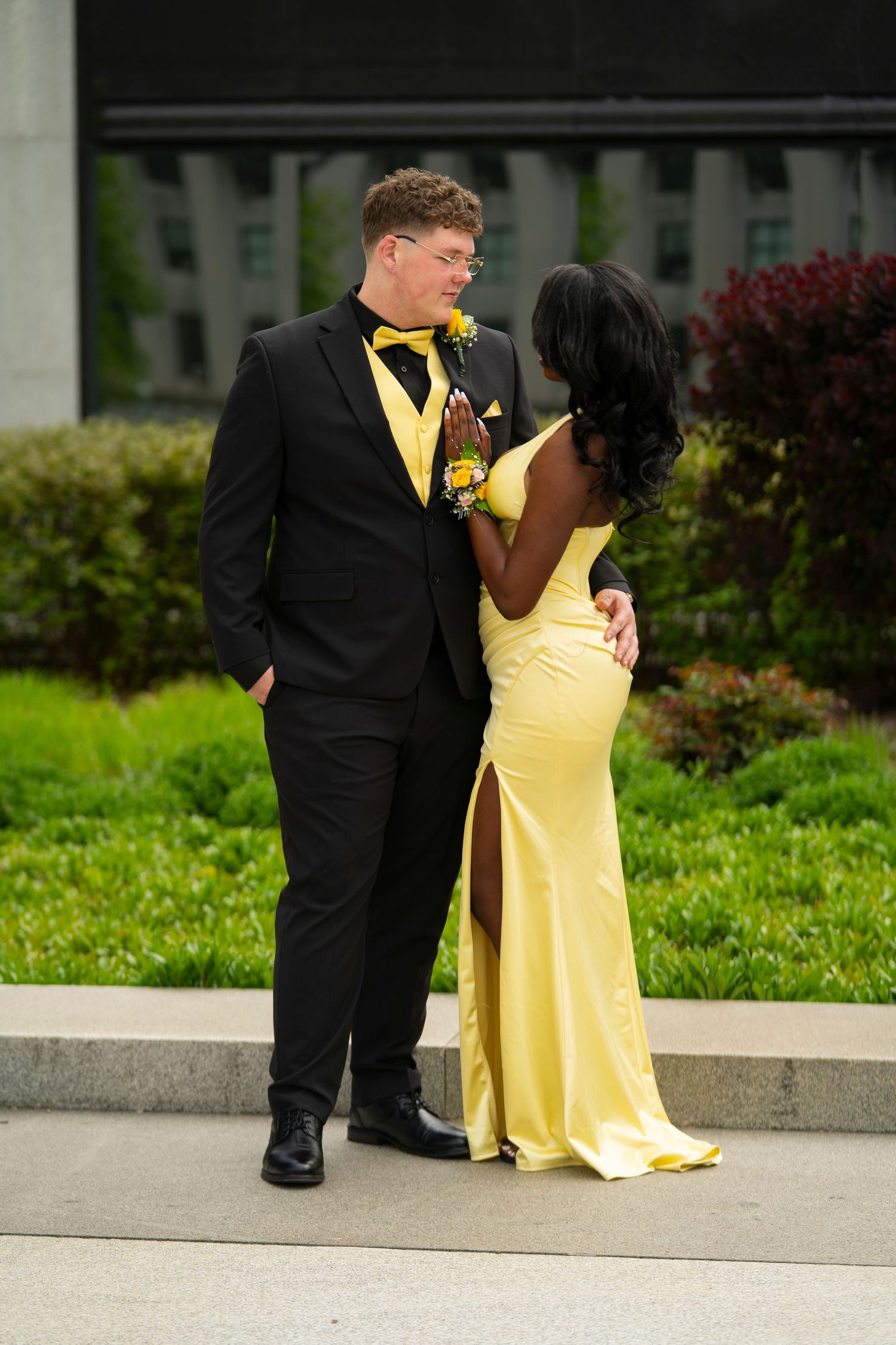 Prom couple in matching yellow and black formal attire poses outdoors on stone steps.