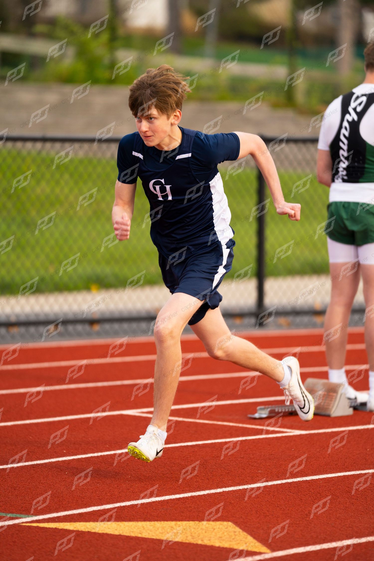 Male high school sprinter in navy CH uniform running on red track.