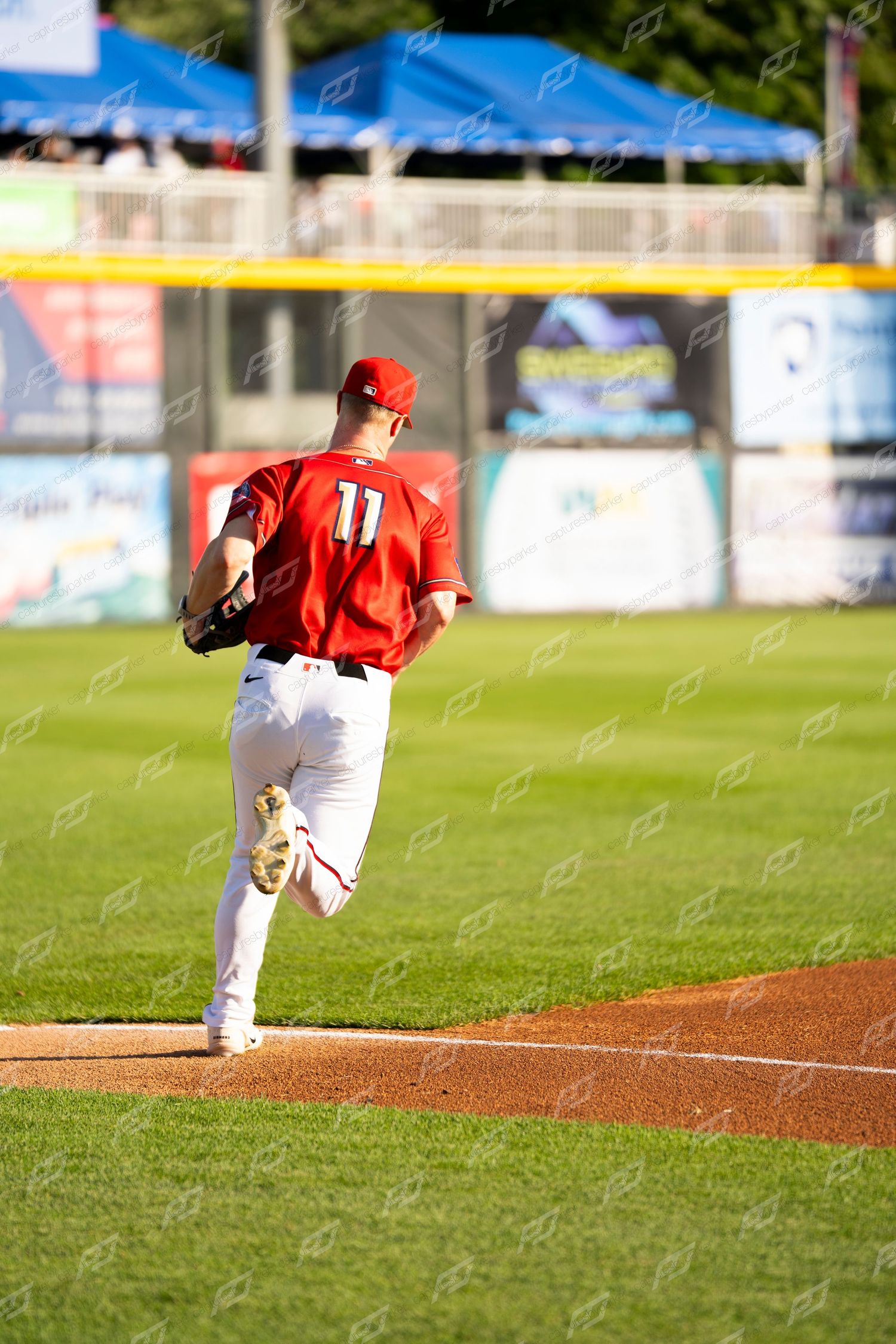 Baseball player wearing number 11 in red uniform jogs toward the pitcher's mound during a day game.