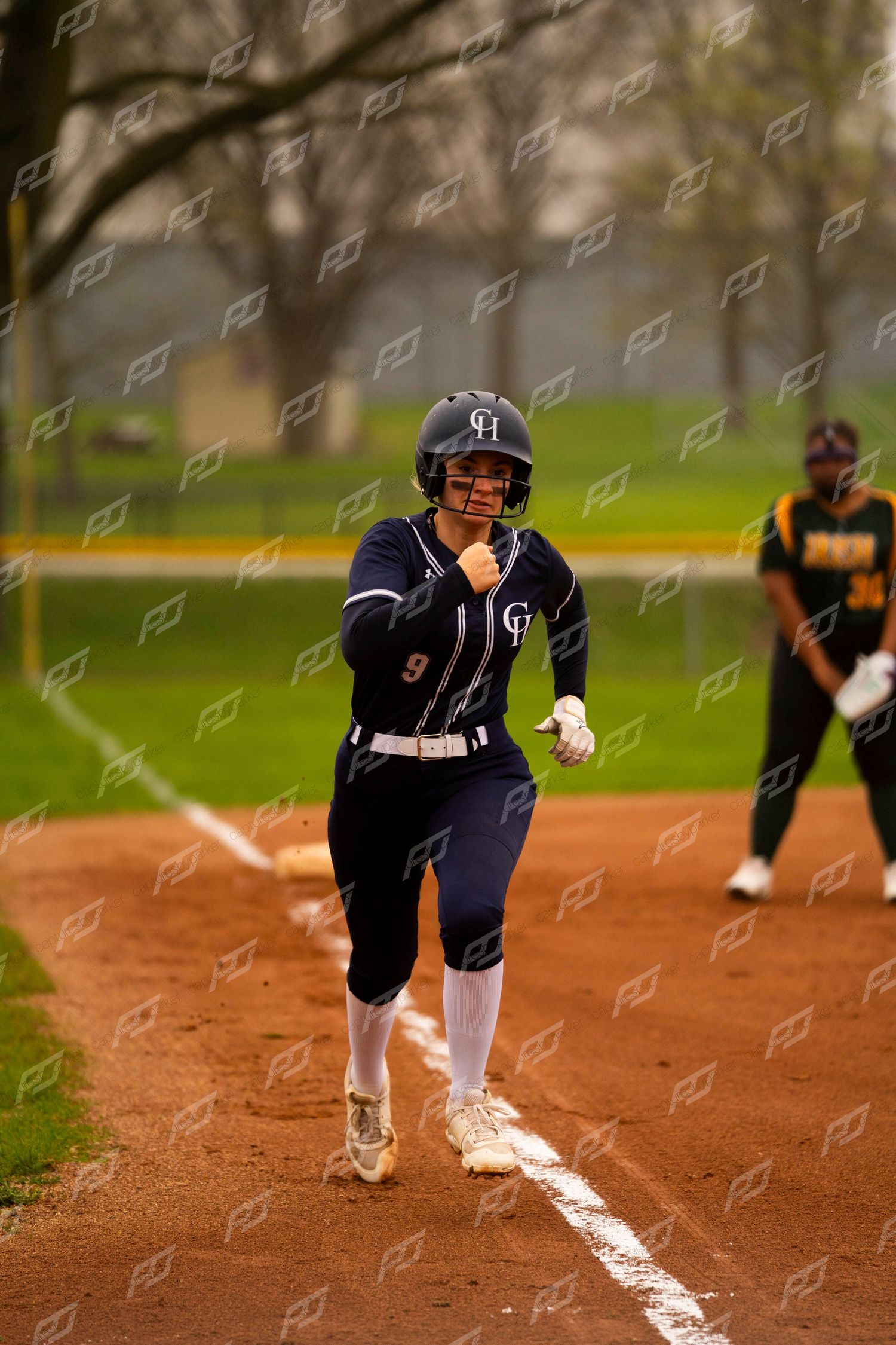 Softball player number 9 in navy uniform runs the bases with determination during an overcast game.