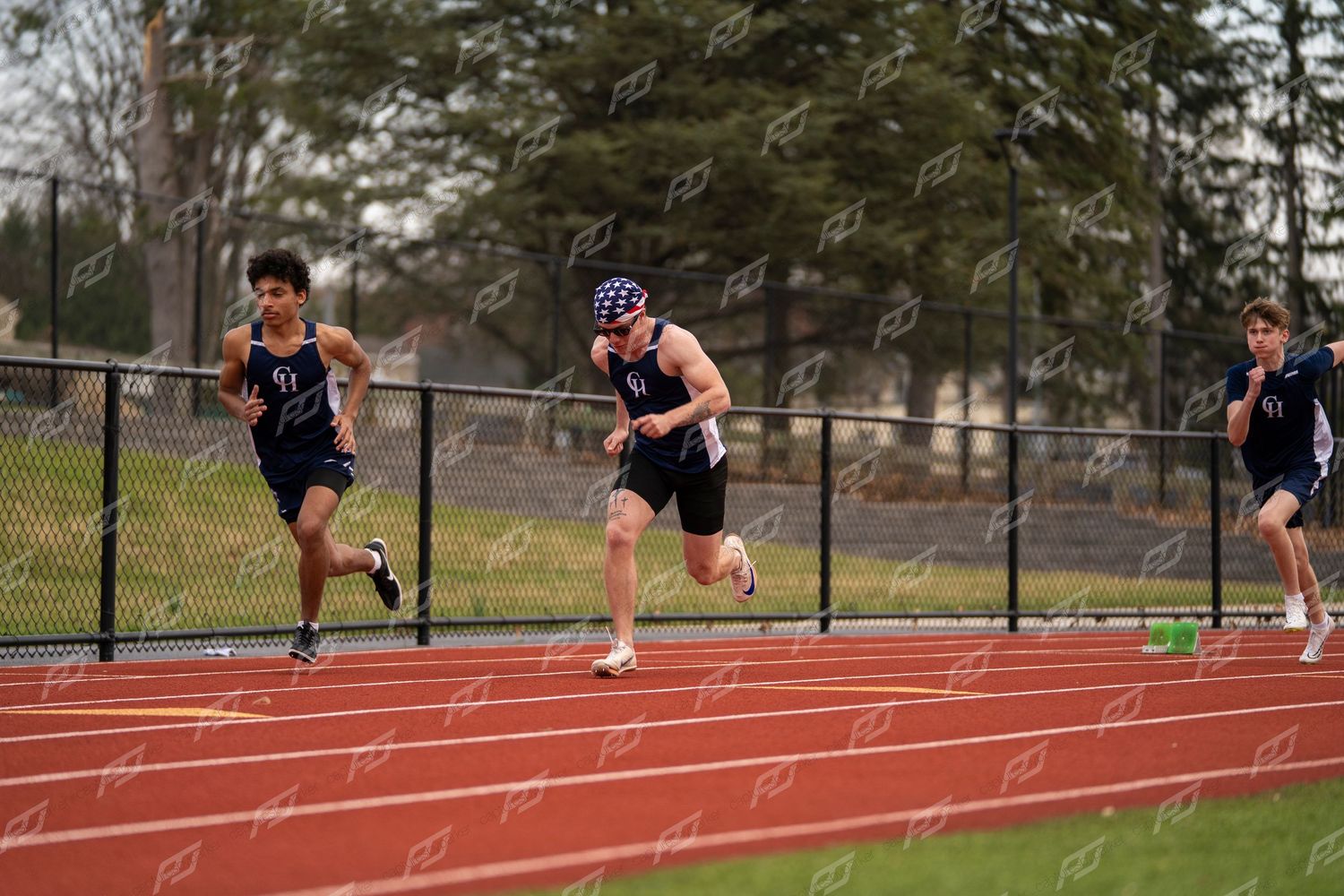 Three male athletes compete in sprint race on red track.