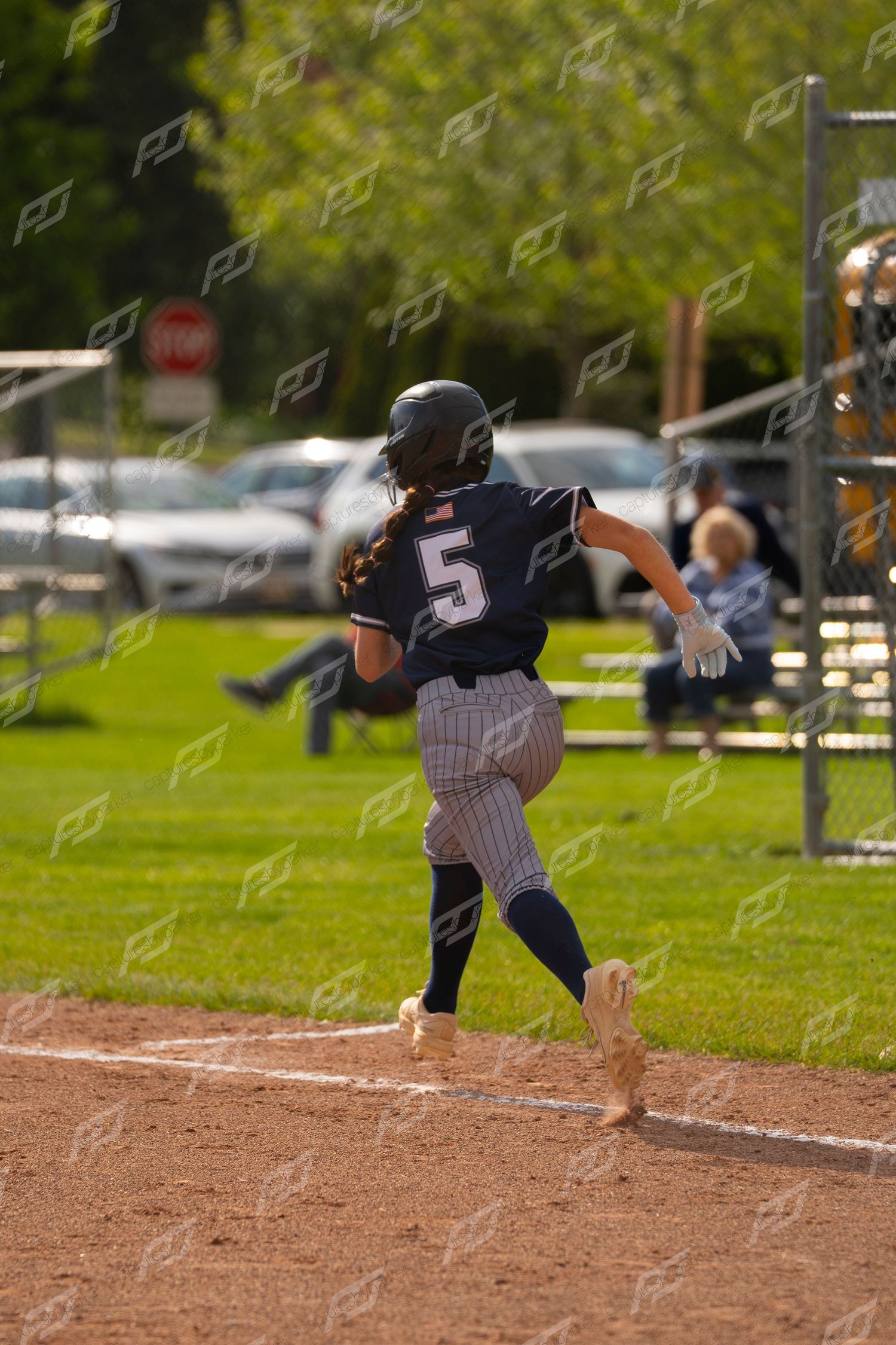 Softball player number 5 in navy pinstripe uniform runs the bases during a game.