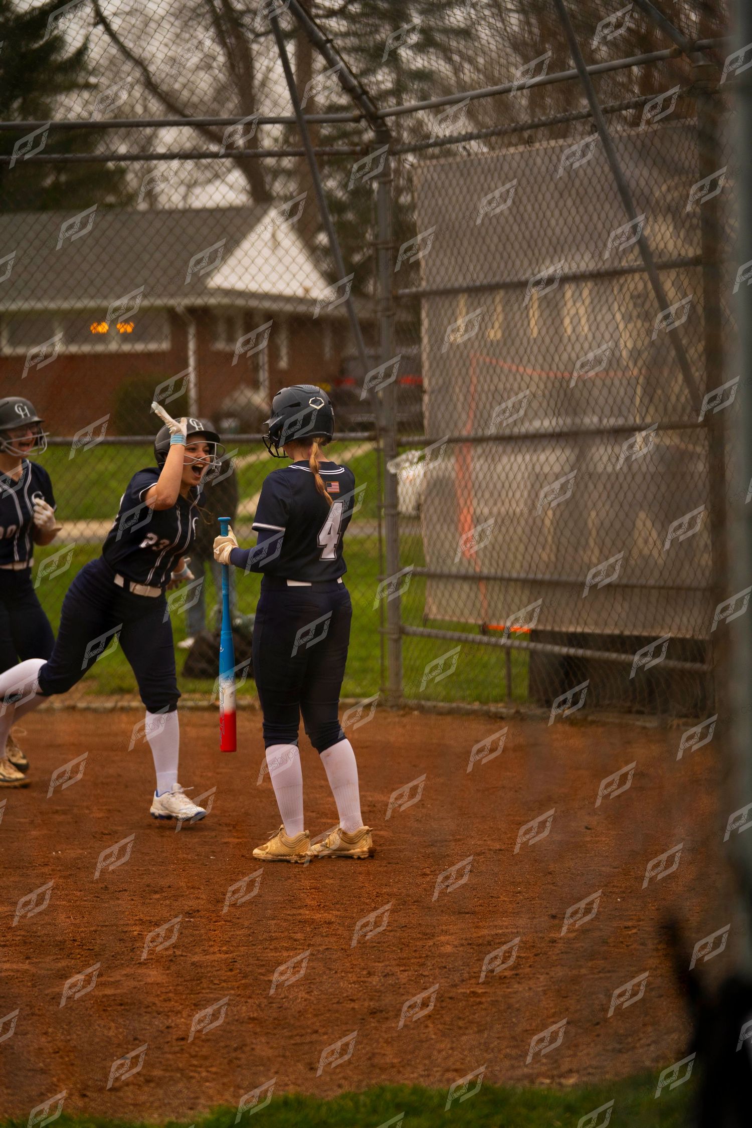 Female softball players in navy uniforms celebrate together near the baseline on a dirt infield.