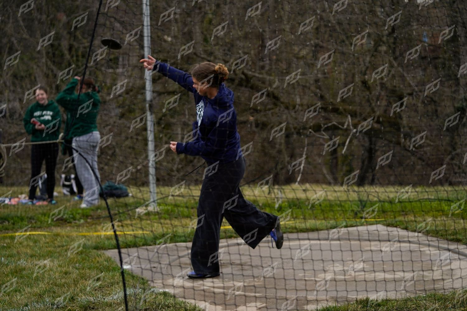 Female athlete in purple uniform releasing a discus during an outdoor track and field meet.