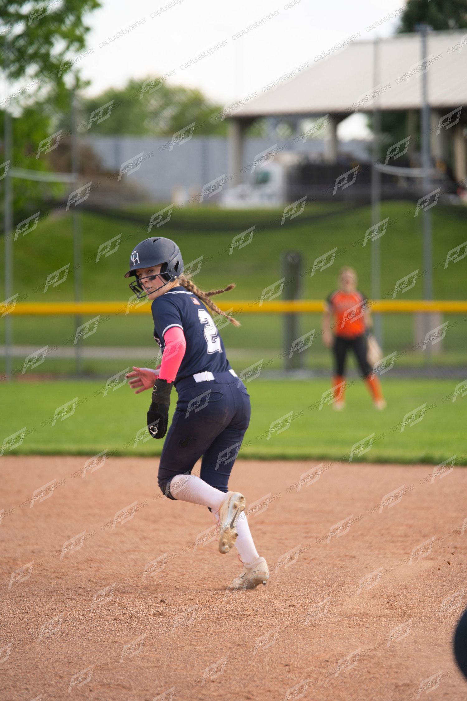 A softball player in navy uniform with red sleeves runs the bases during an evening game.
