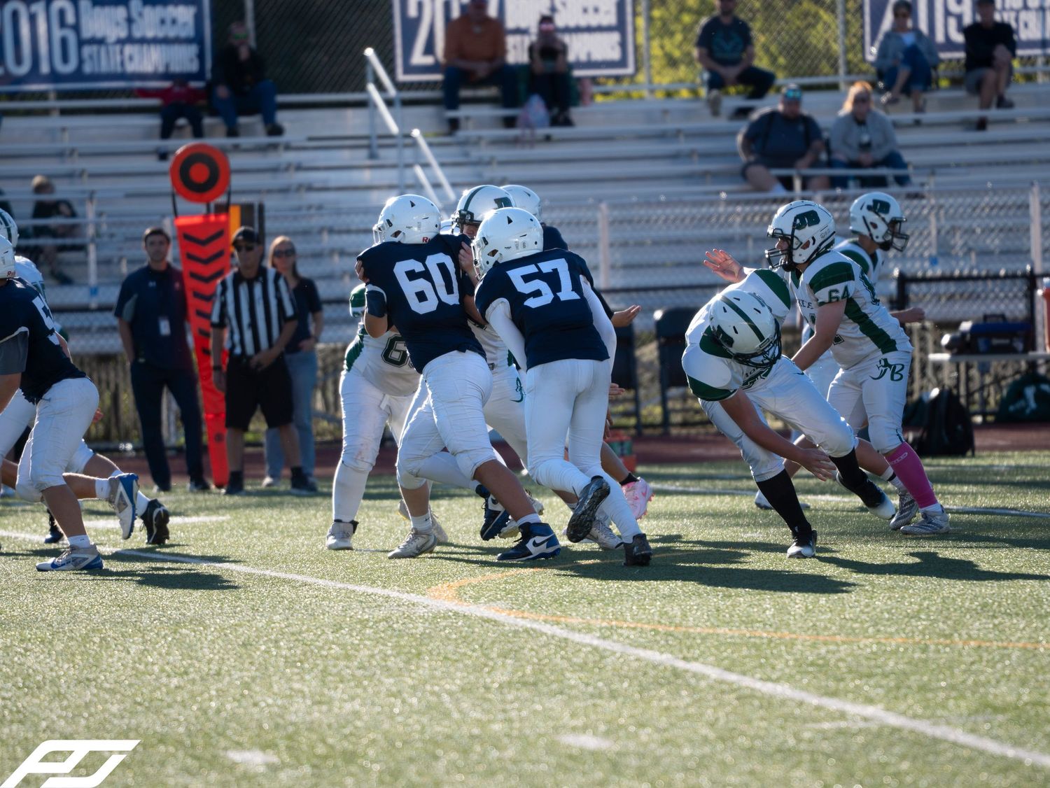 Youth football players in navy uniforms compete on a sunny field during a game.