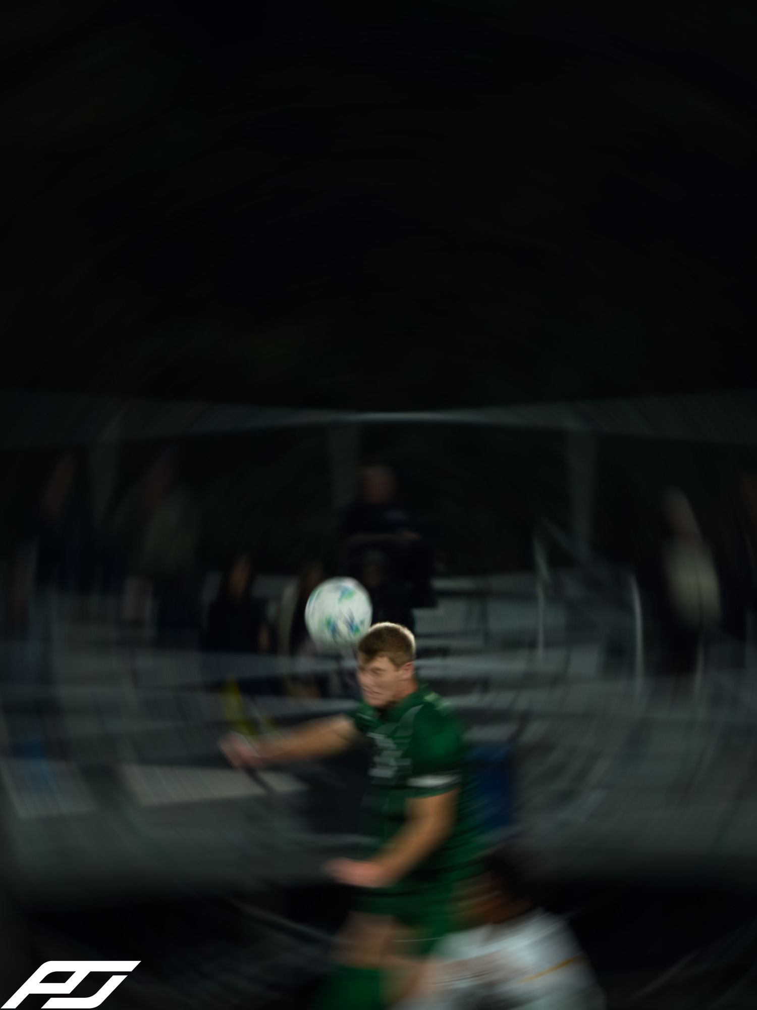 Soccer player in green jersey heads the ball during a nighttime match.
