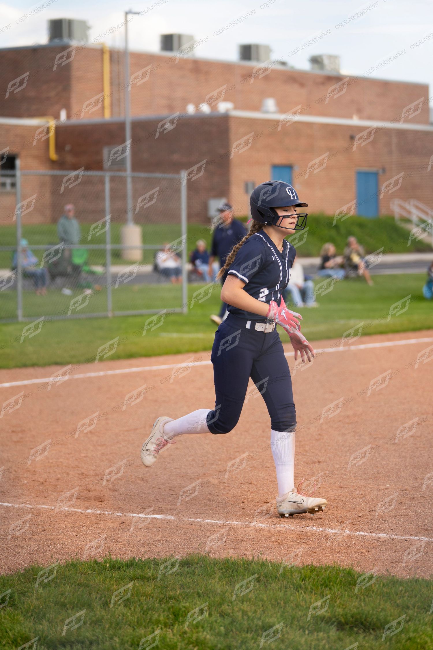 A softball player in navy uniform number 23 runs the bases during an evening game.