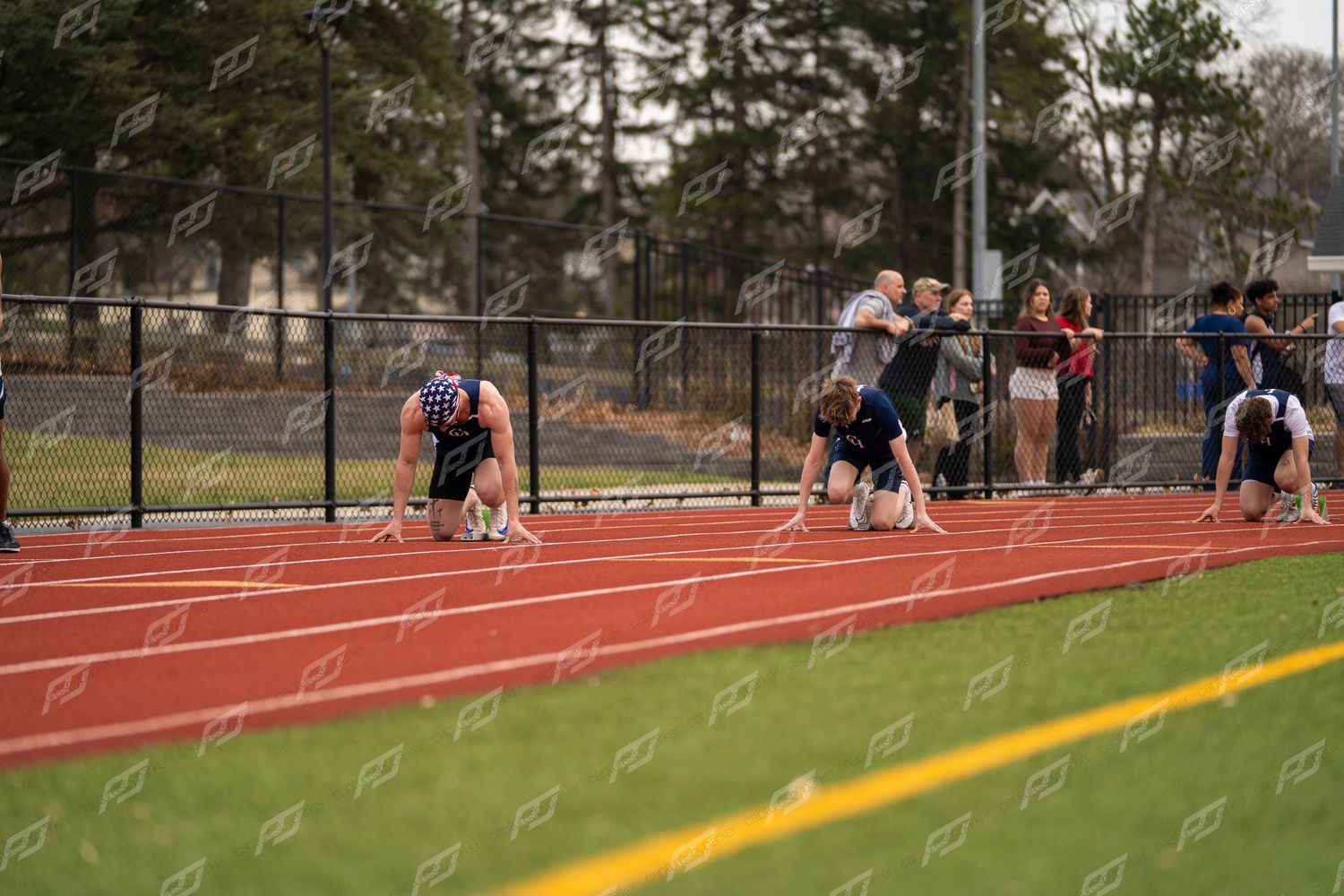 Multiple athletes in starting blocks on red track preparing to sprint.