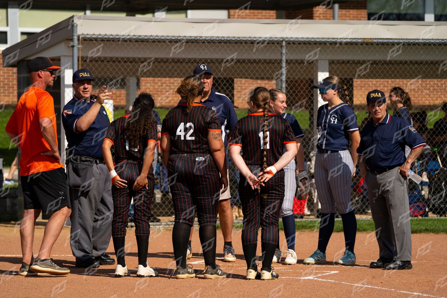 Softball team huddles together on field with coaches and umpire during a game.