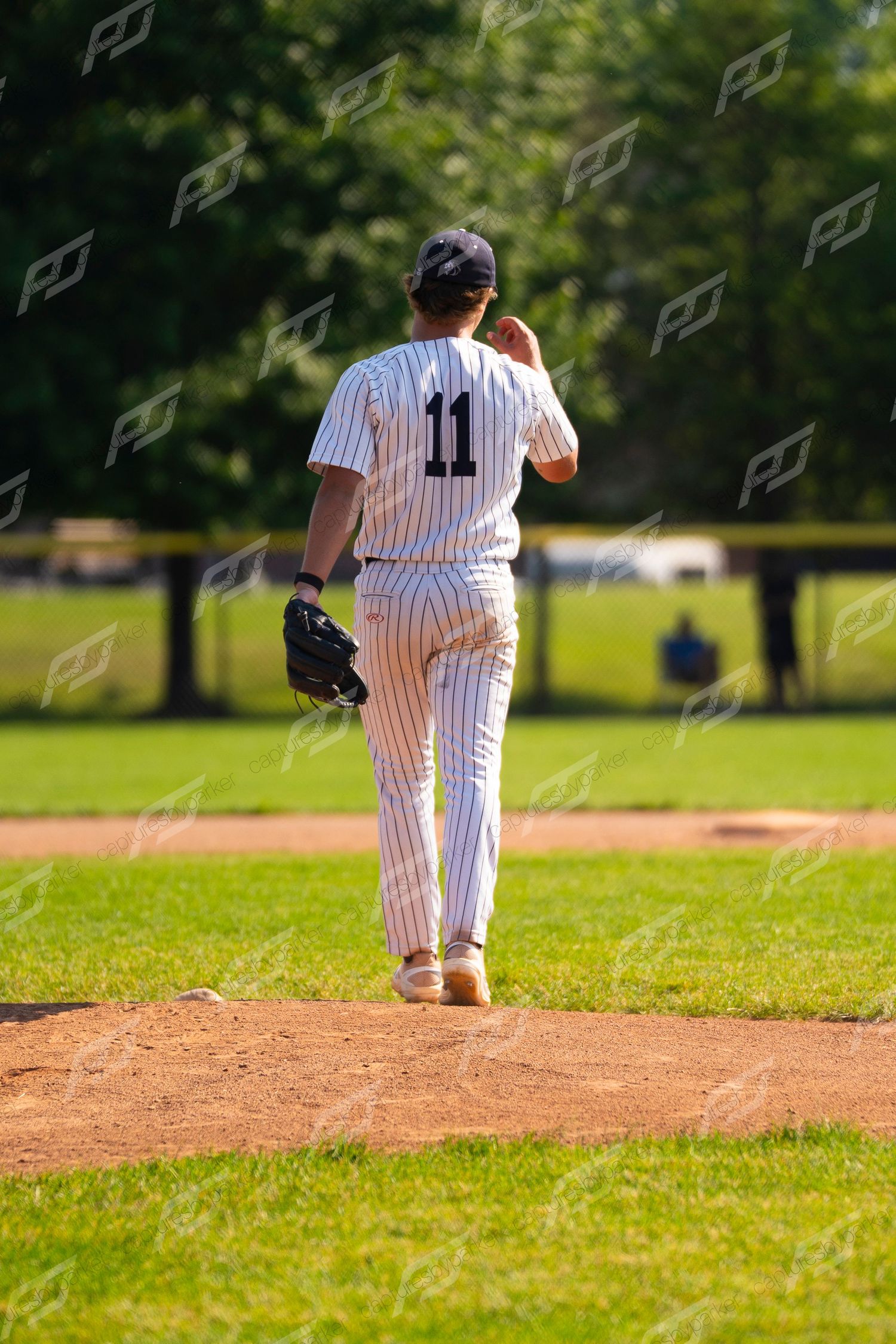 Baseball player #11 in pinstripe uniform walking back to the pitching mound during a game.