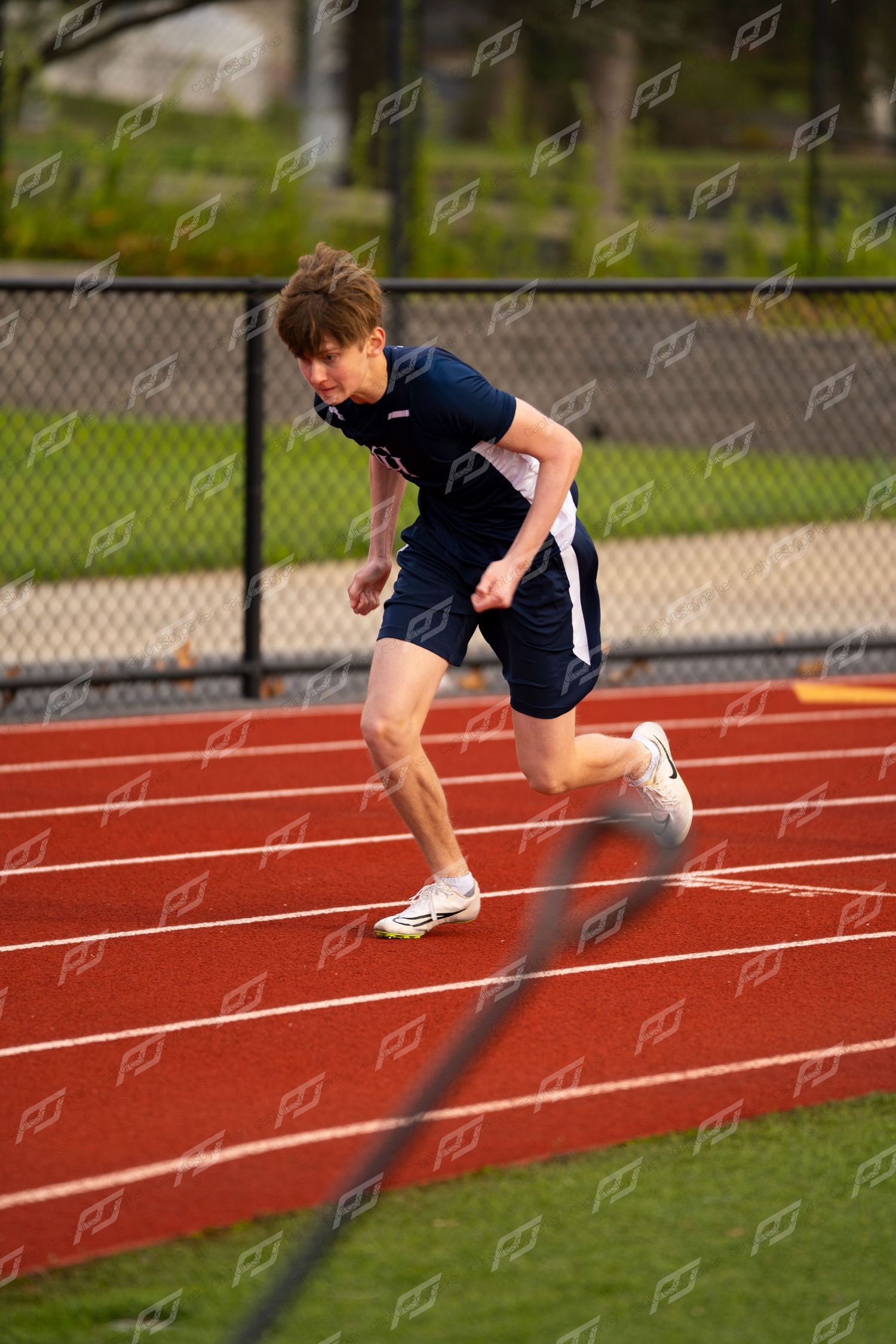 Young male track athlete sprinting on red outdoor track in navy uniform.