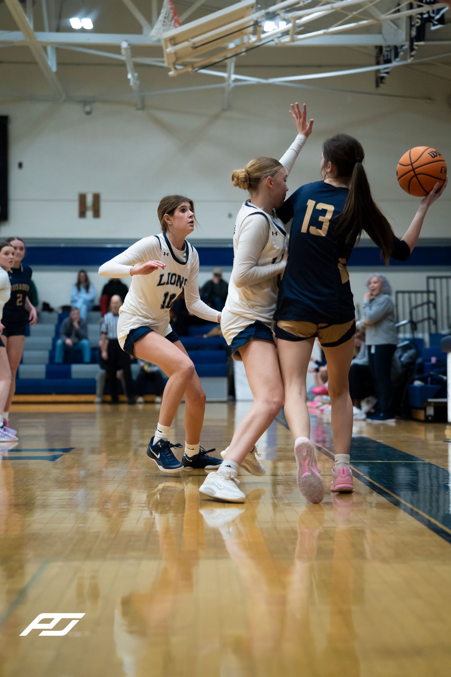 Lions players defend an opponent driving to the basket during a girls basketball game.