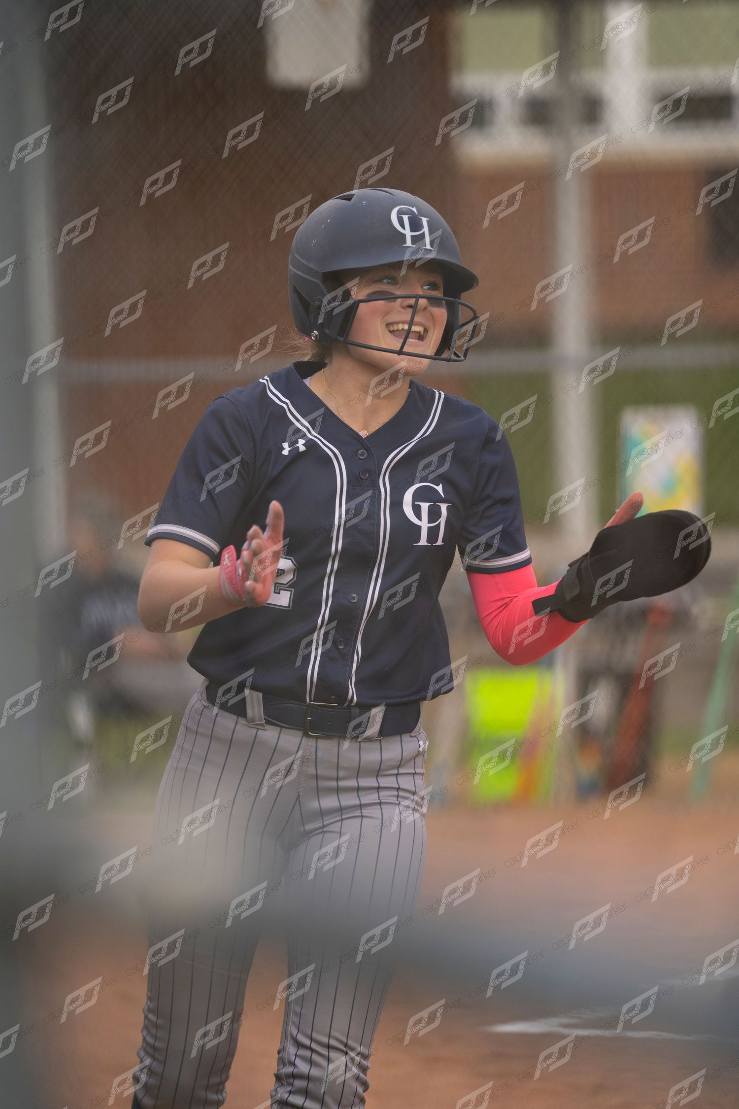 Female softball player in navy CH uniform and helmet claps hands near home plate during game.
