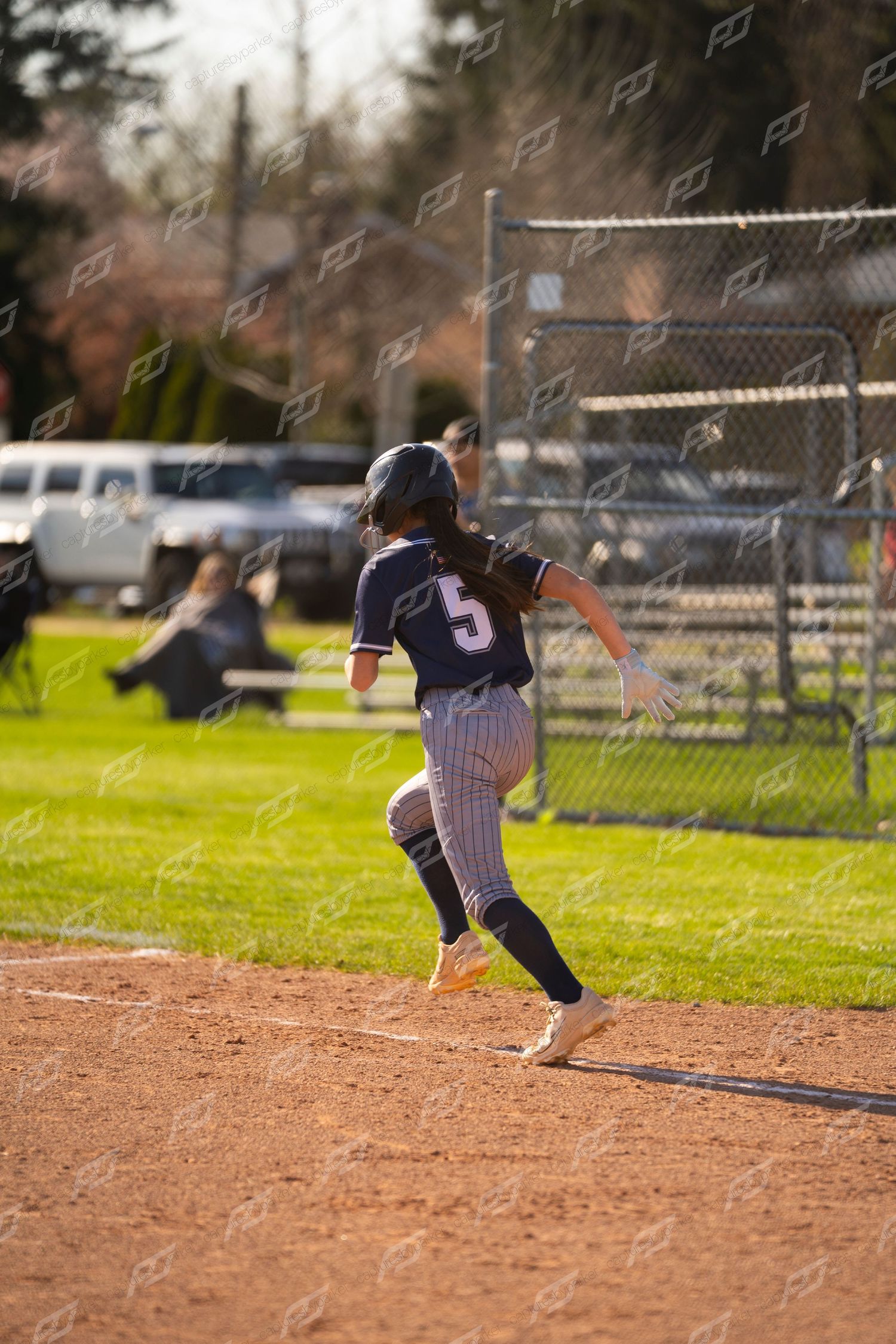 Female softball player #5 in navy pinstripe uniform sprinting down baseline during outdoor game.