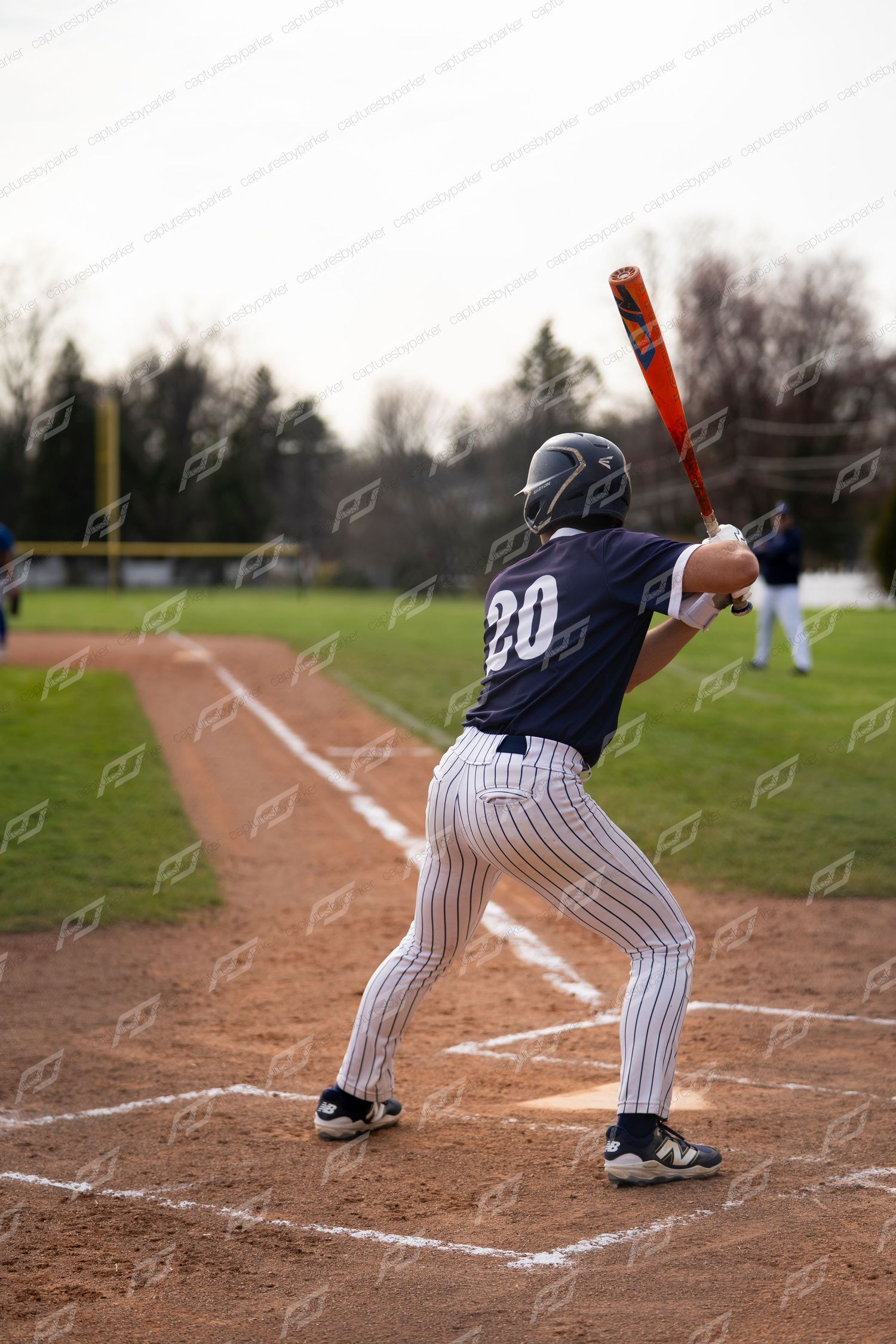 Baseball player #20 in navy and white pinstripe uniform stands ready to bat at home plate.