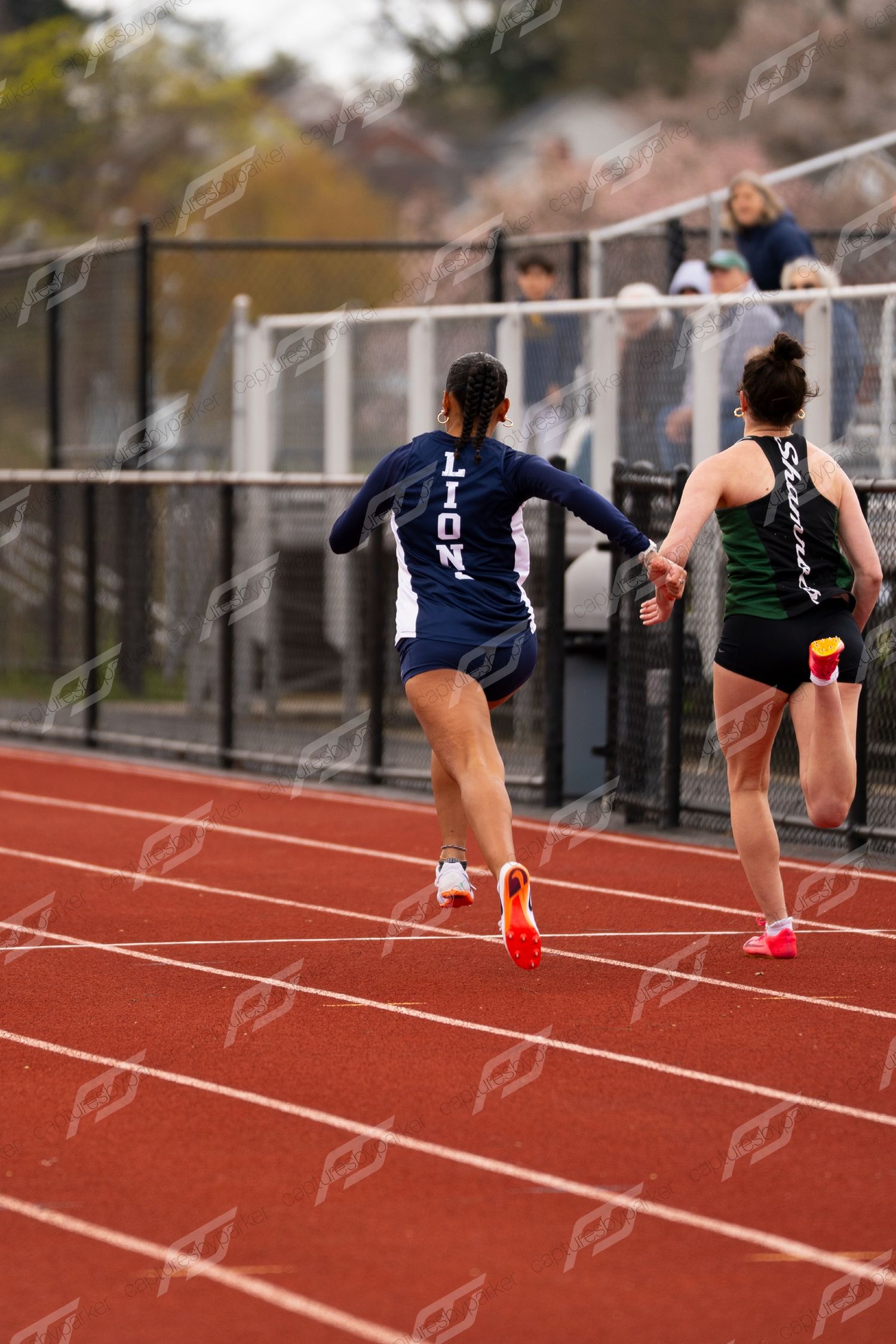 Female Lions athlete and competitor sprint down red track during outdoor track and field meet.