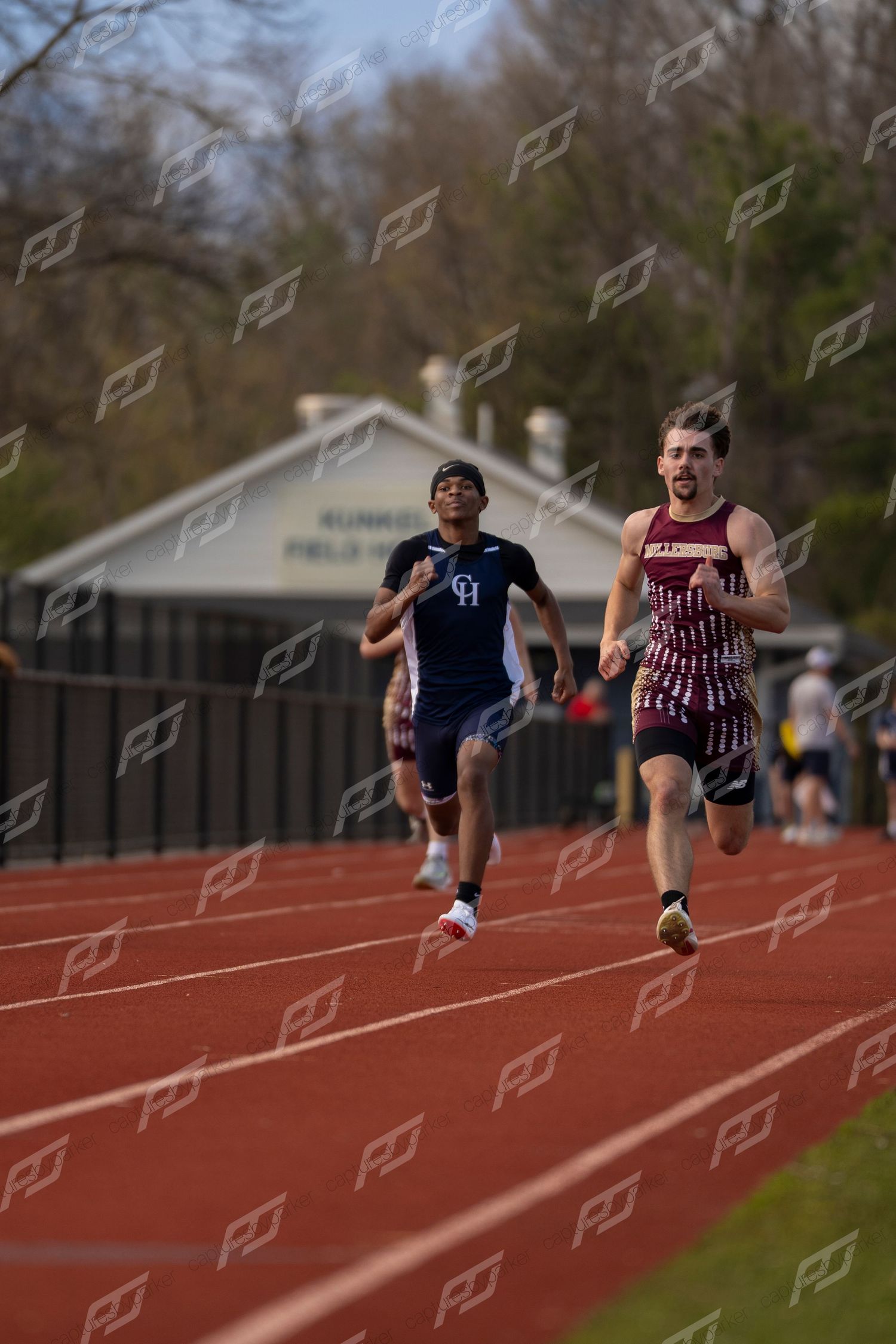 Two male runners compete in sprint race on red track, CH athlete in navy uniform.