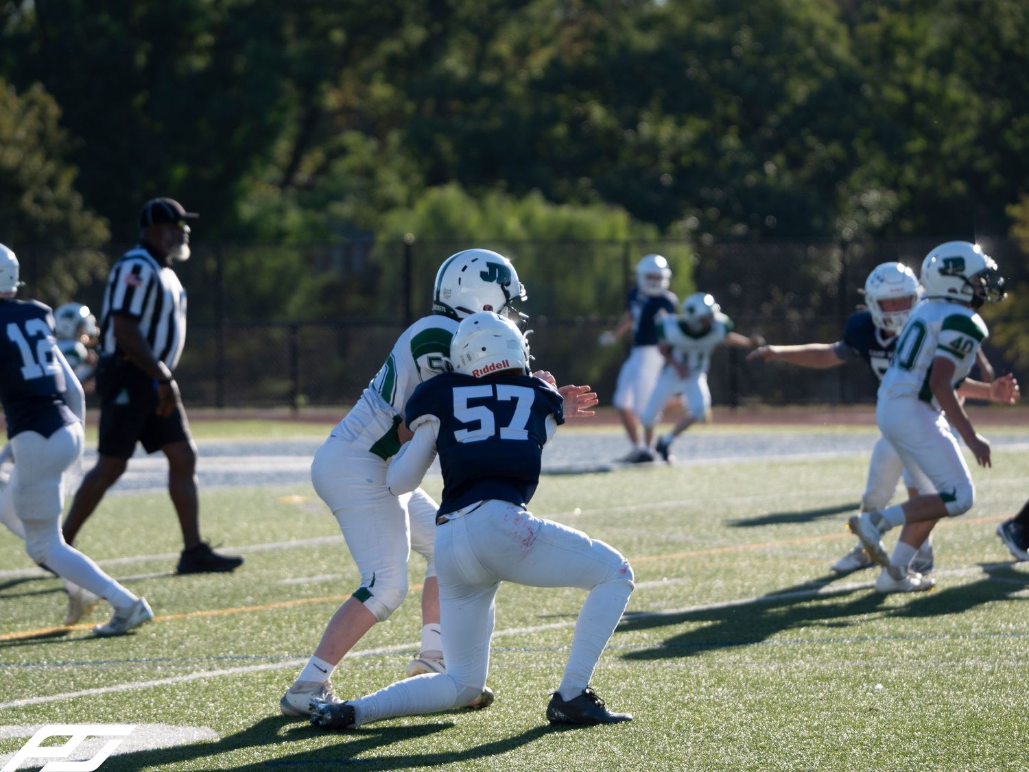 Youth football player number 57 in navy uniform engages in a blocking drill during a game.