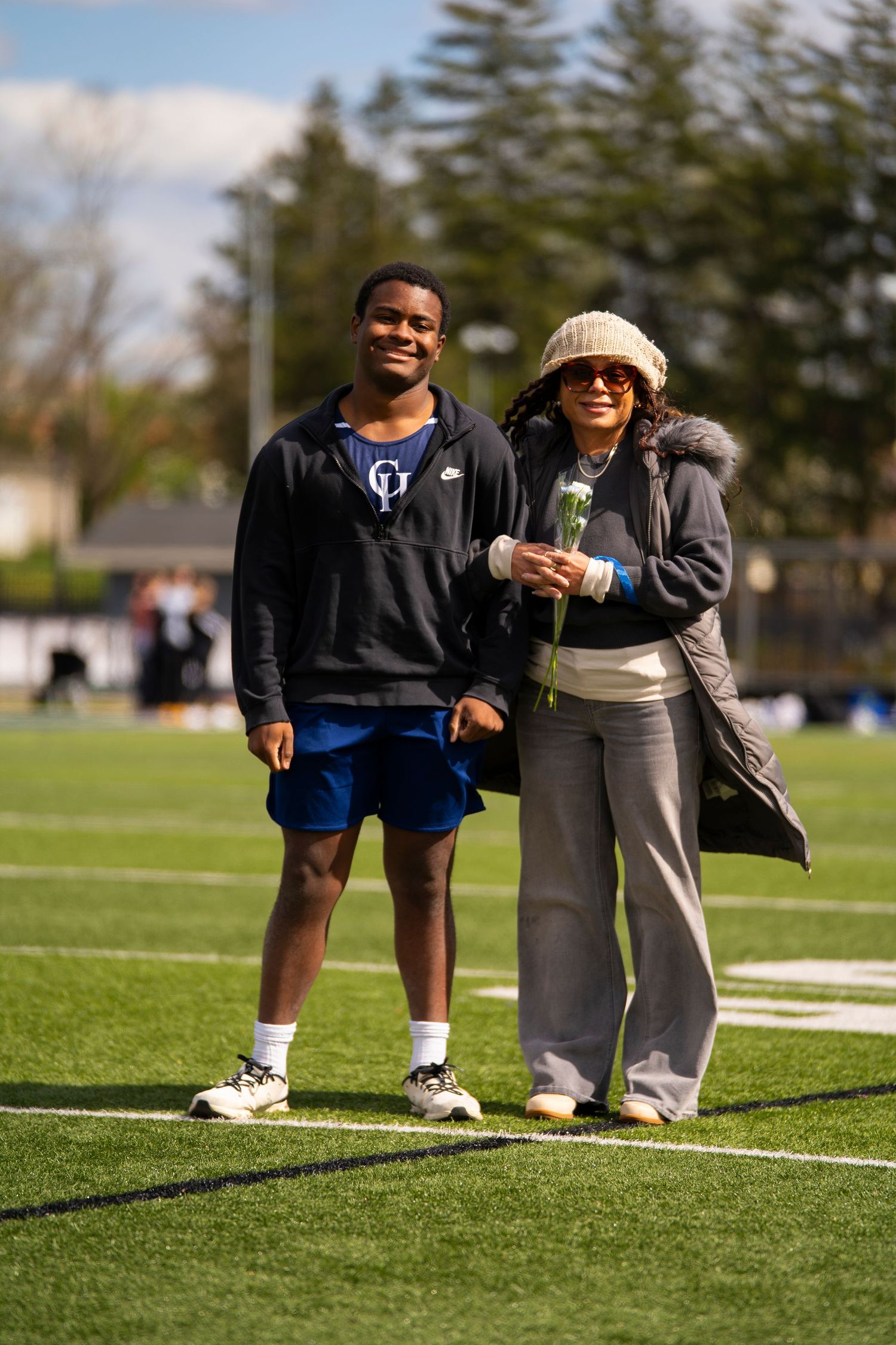 A male athlete and a woman pose together on a football field during senior day.