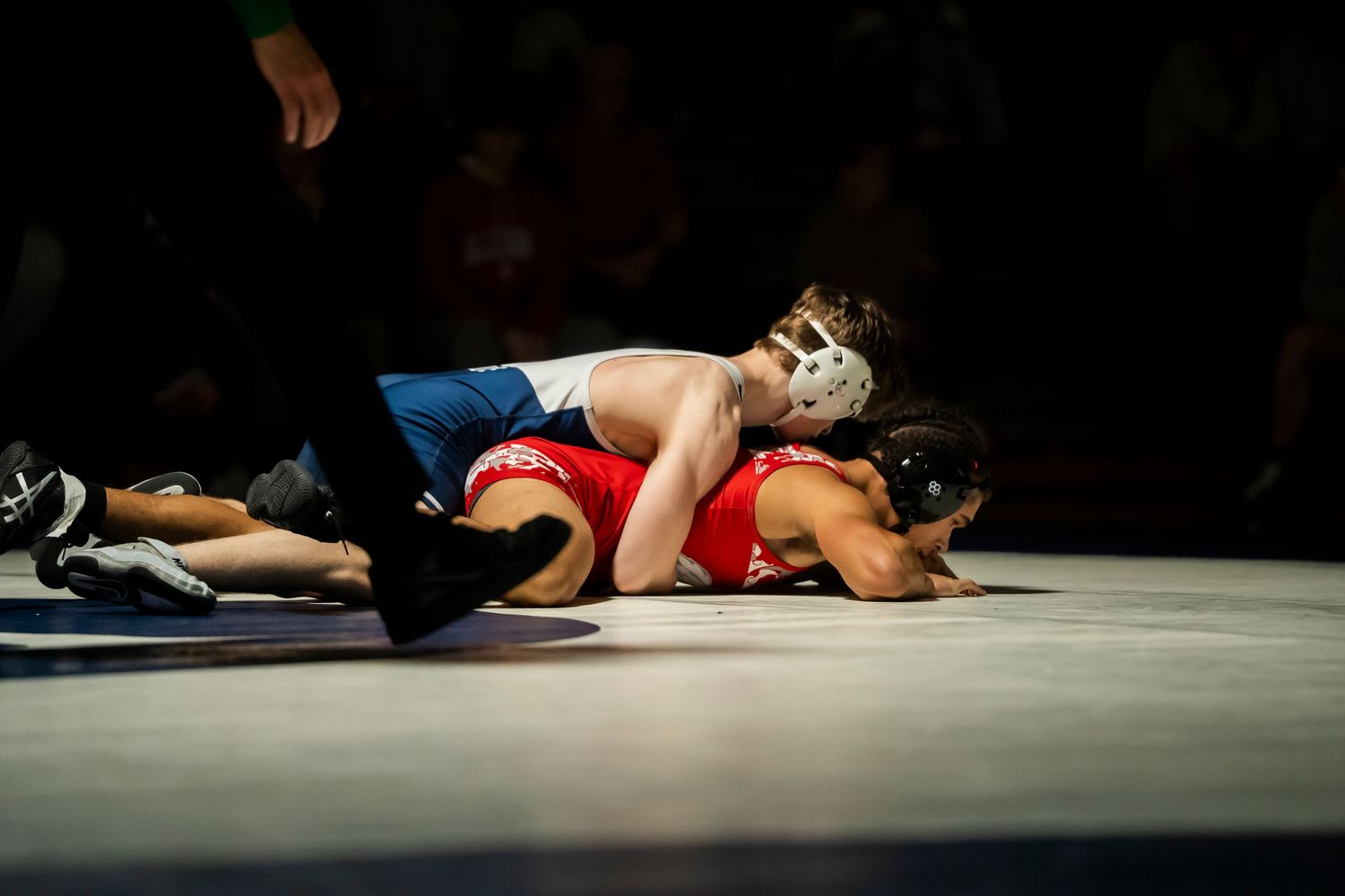 A wrestler in blue singlet pins opponent in red to the mat during a competitive wrestling match.