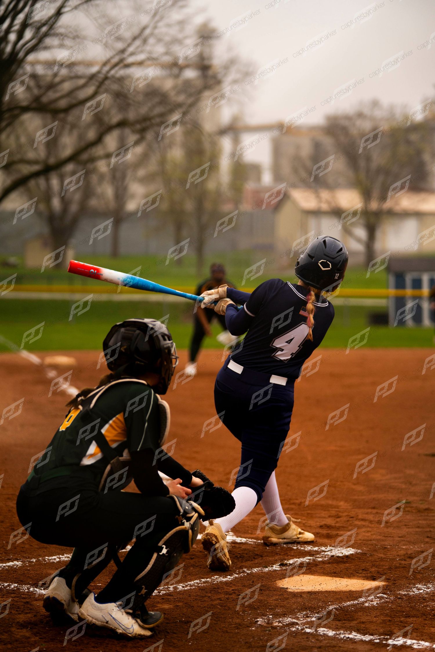 Softball batter in navy uniform swinging a colorful bat with catcher crouching at home plate.