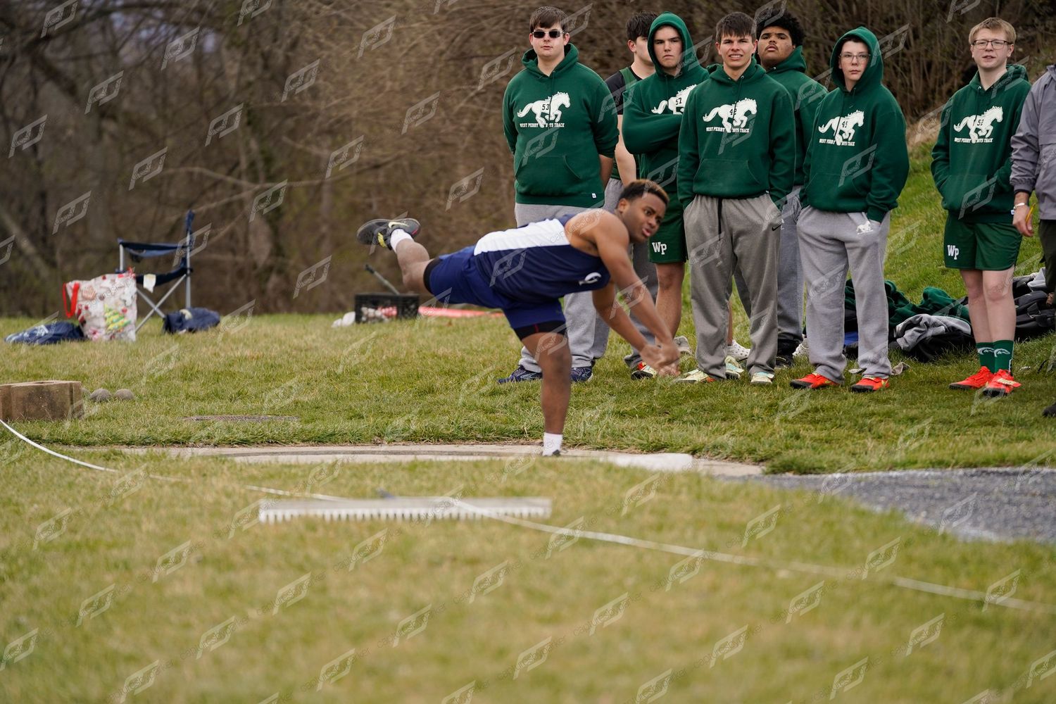 Male athlete leans forward releasing a discus throw at an outdoor high school track and field event.