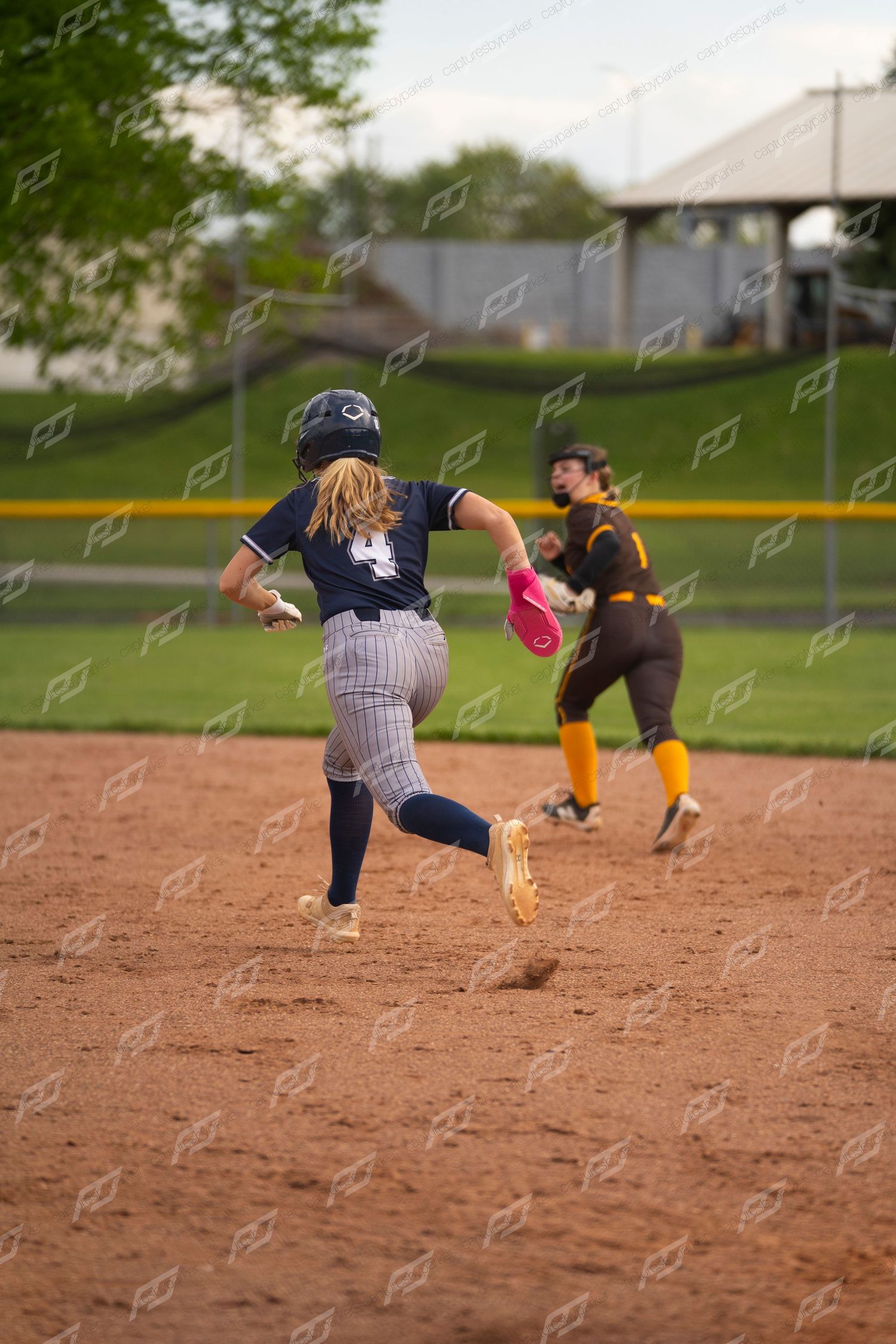 Softball player number 4 runs the bases as an opposing fielder prepares to throw.