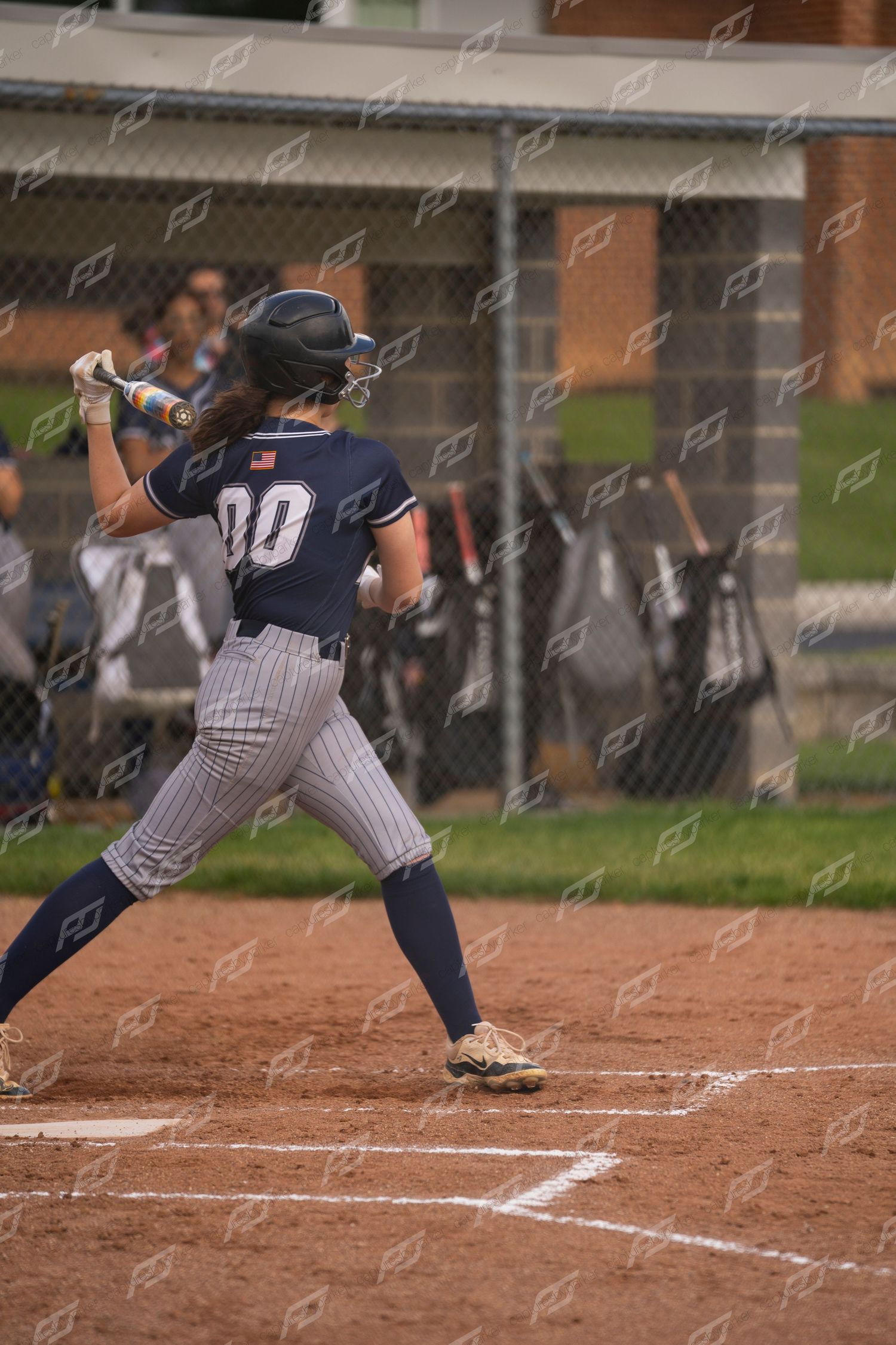 Female softball player number 00 in navy pinstripe uniform swings bat during outdoor game.